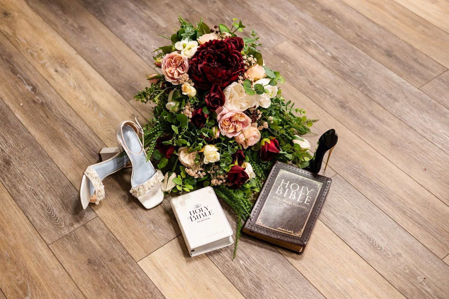 Wedding detail flatlay with floral arrangements and decorative items on rustic wooden flooring.