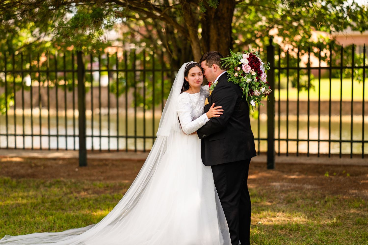 Outdoor wedding portraits captured in a garden setting with iron fencing and natural greenery.