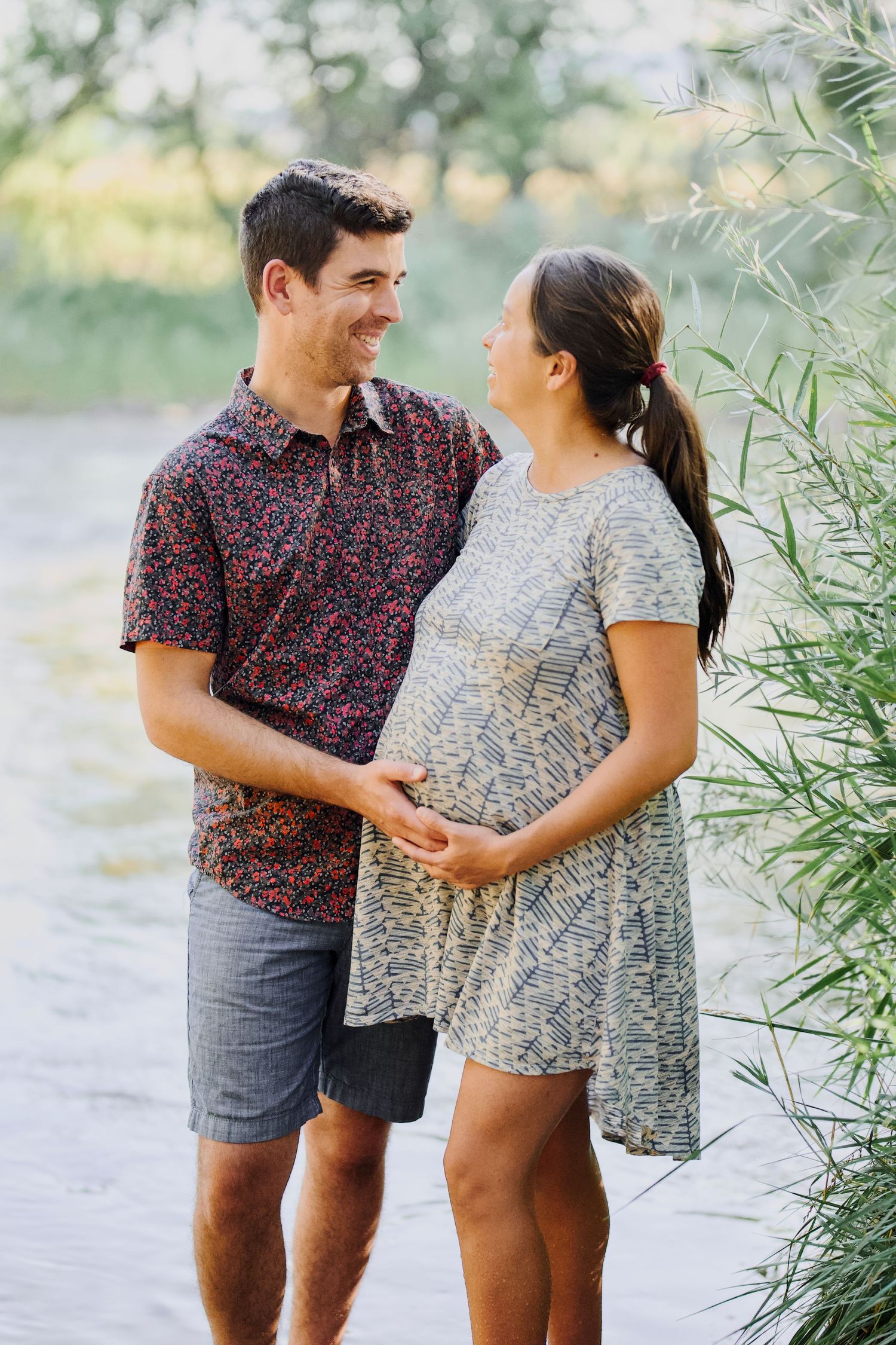 A maternity portrait of a married couple outdoors with trees in the background by the Poudre River in Fort Collins, Colorado.