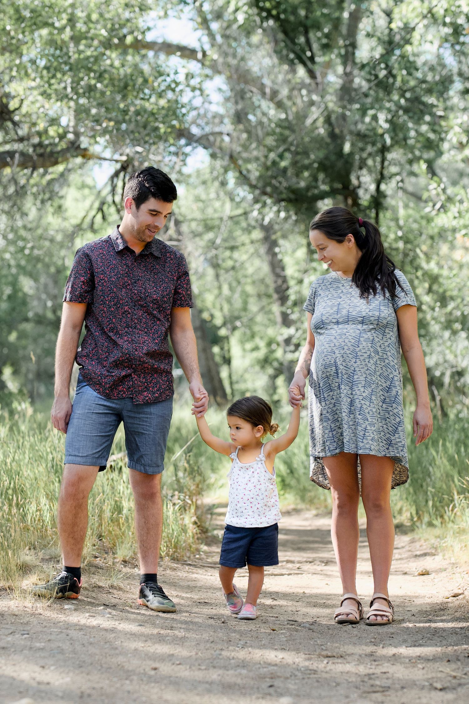 A portrait of a family of three outdoors with trees in the background by the Poudre River in Fort Collins, Colorado.