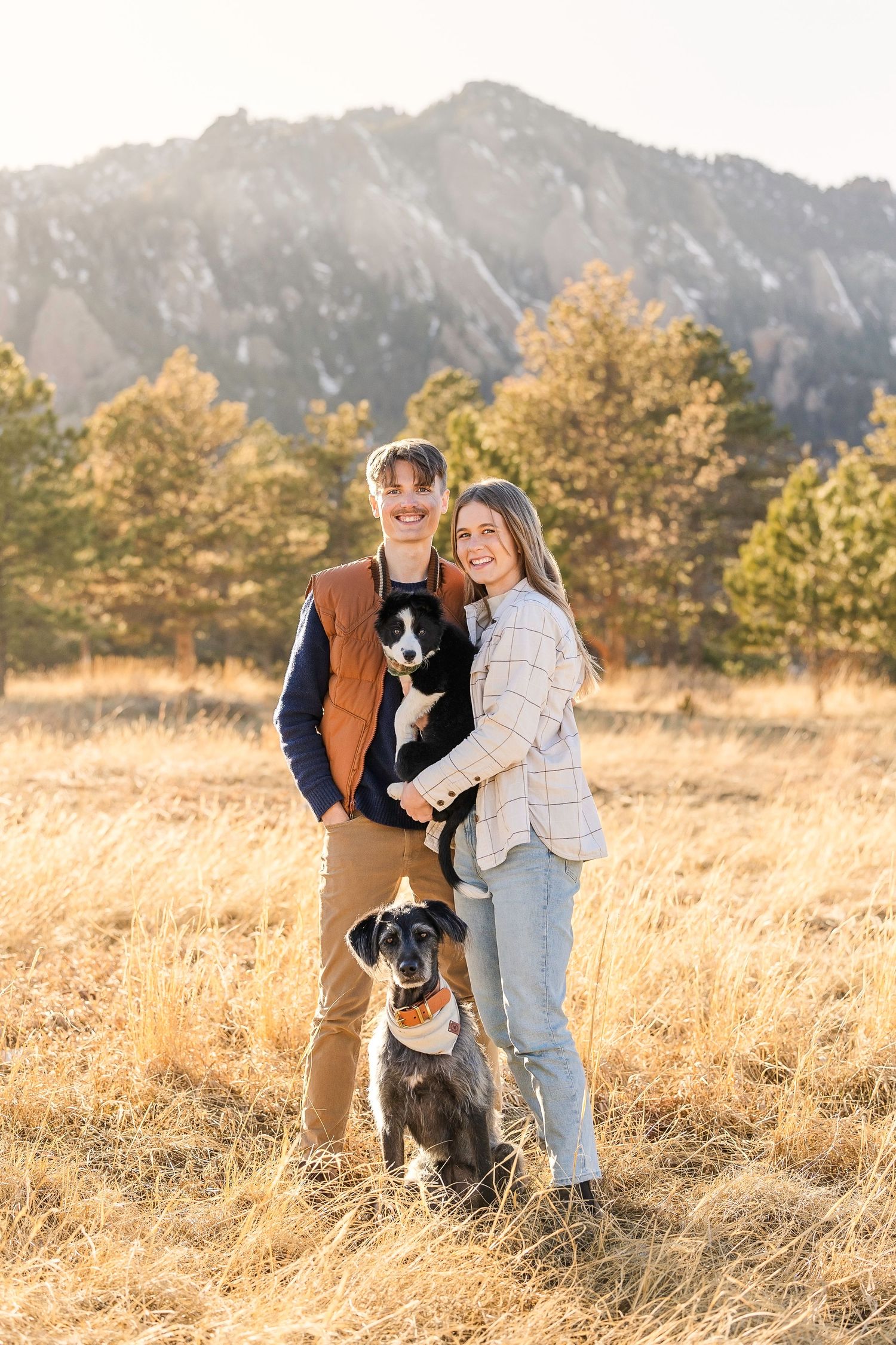Family and dog enjoying autumn afternoon in golden field with mountain backdrop.
