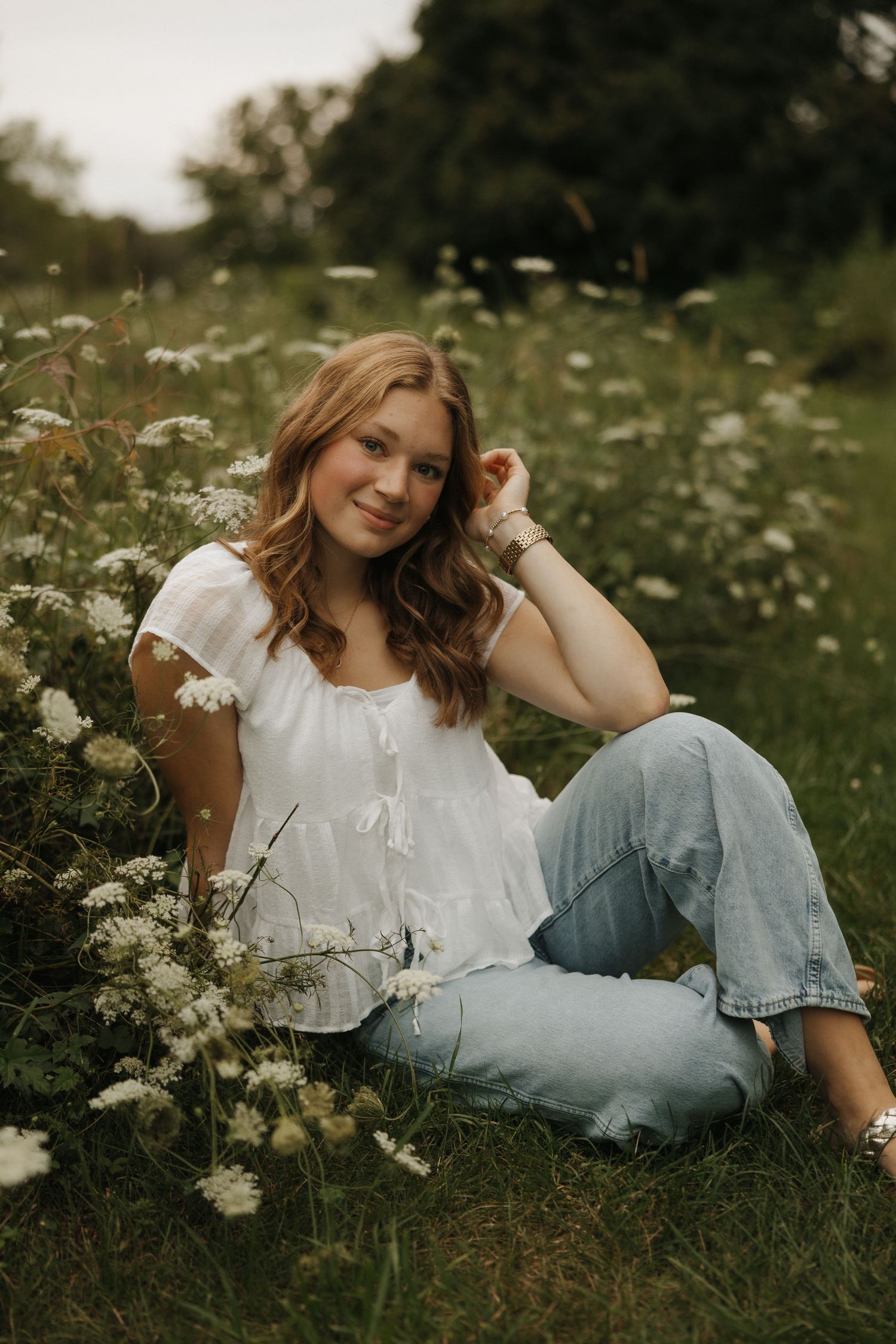 A dreamy summer portrait of someone in a white blouse and jeans lounging in a wildflower meadow at golden hour.