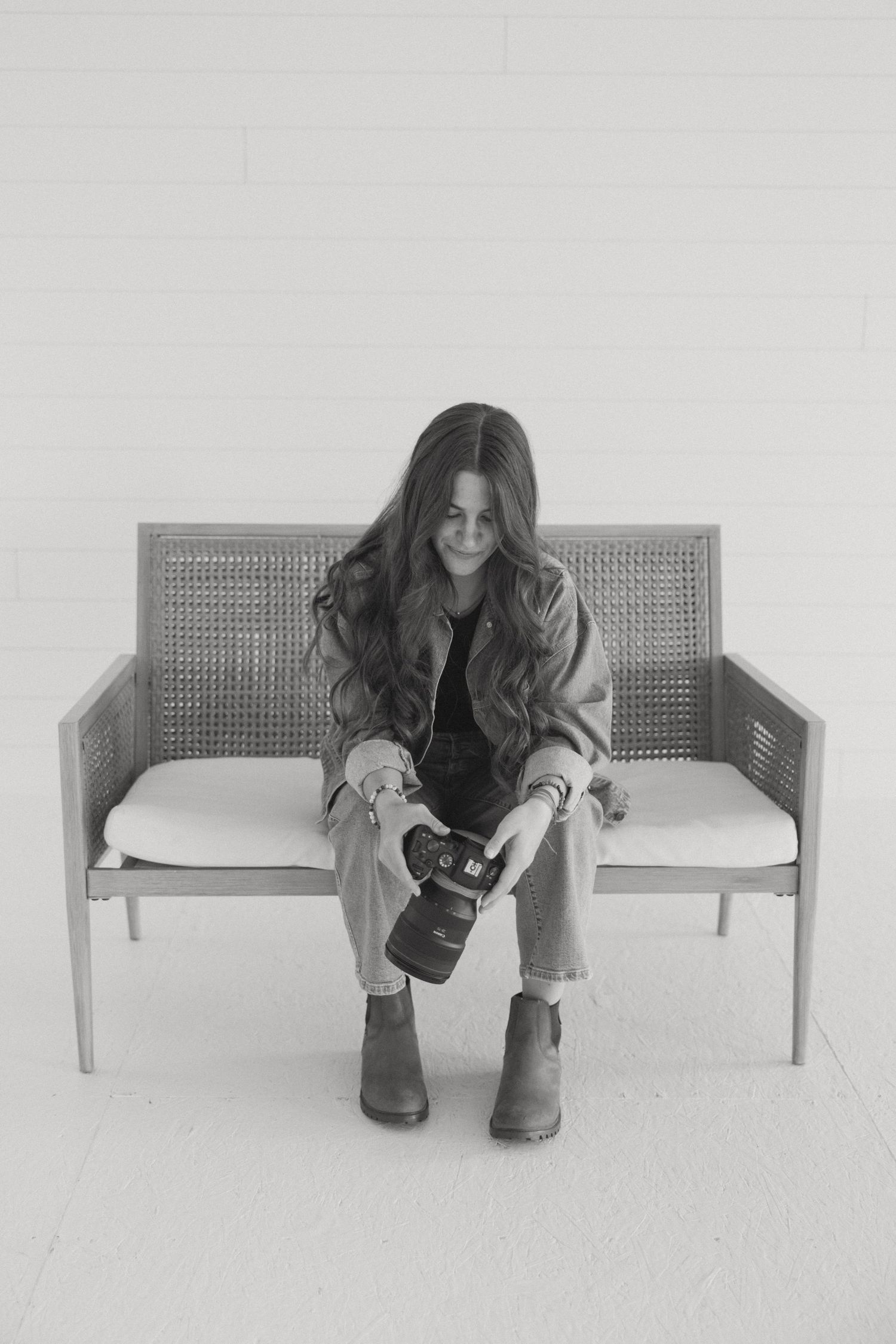 Person sitting on woven bench with camera in black and white photography.