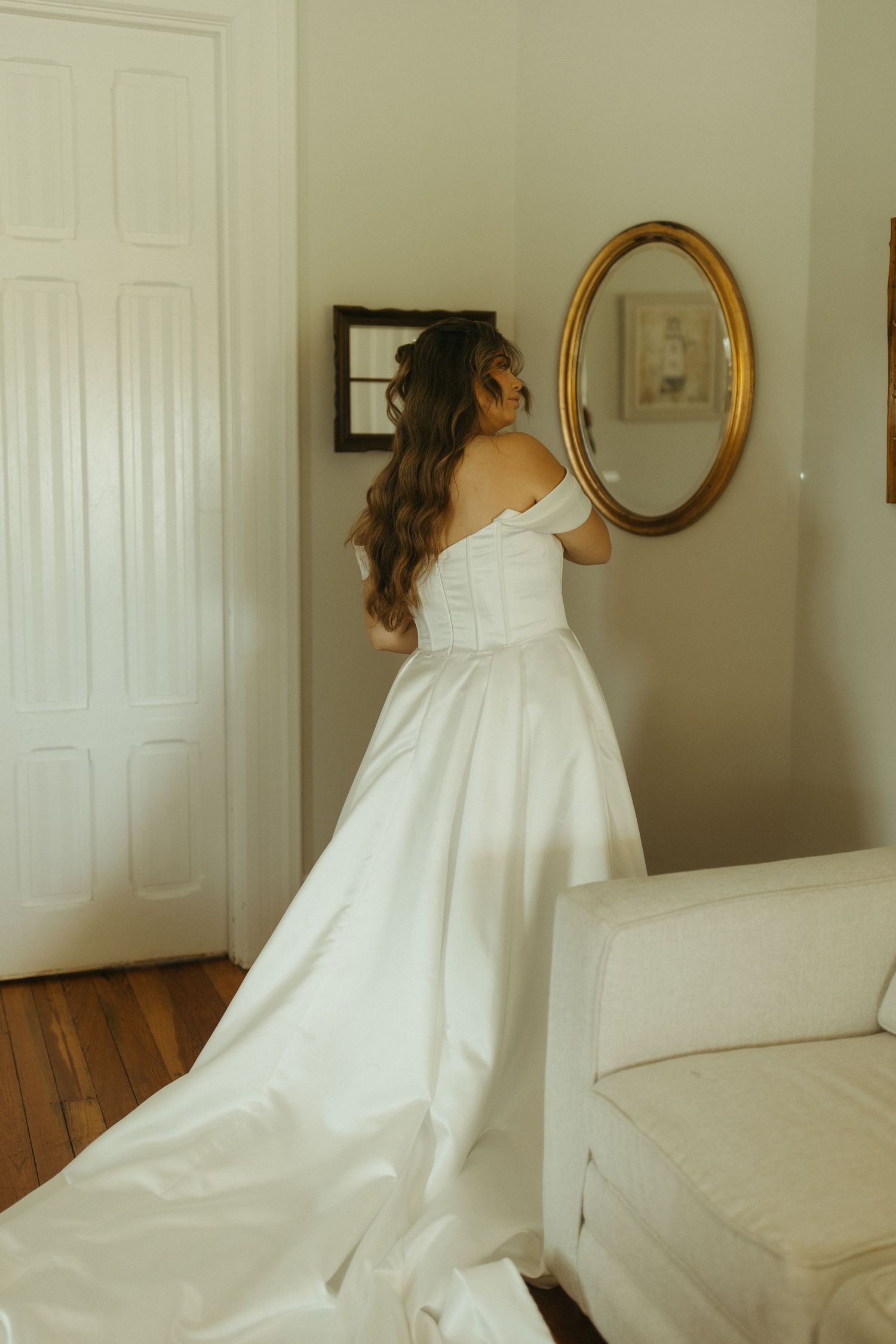 A figure in a flowing white dress twirls gracefully in a sunlit room with hardwood floors and white walls.
