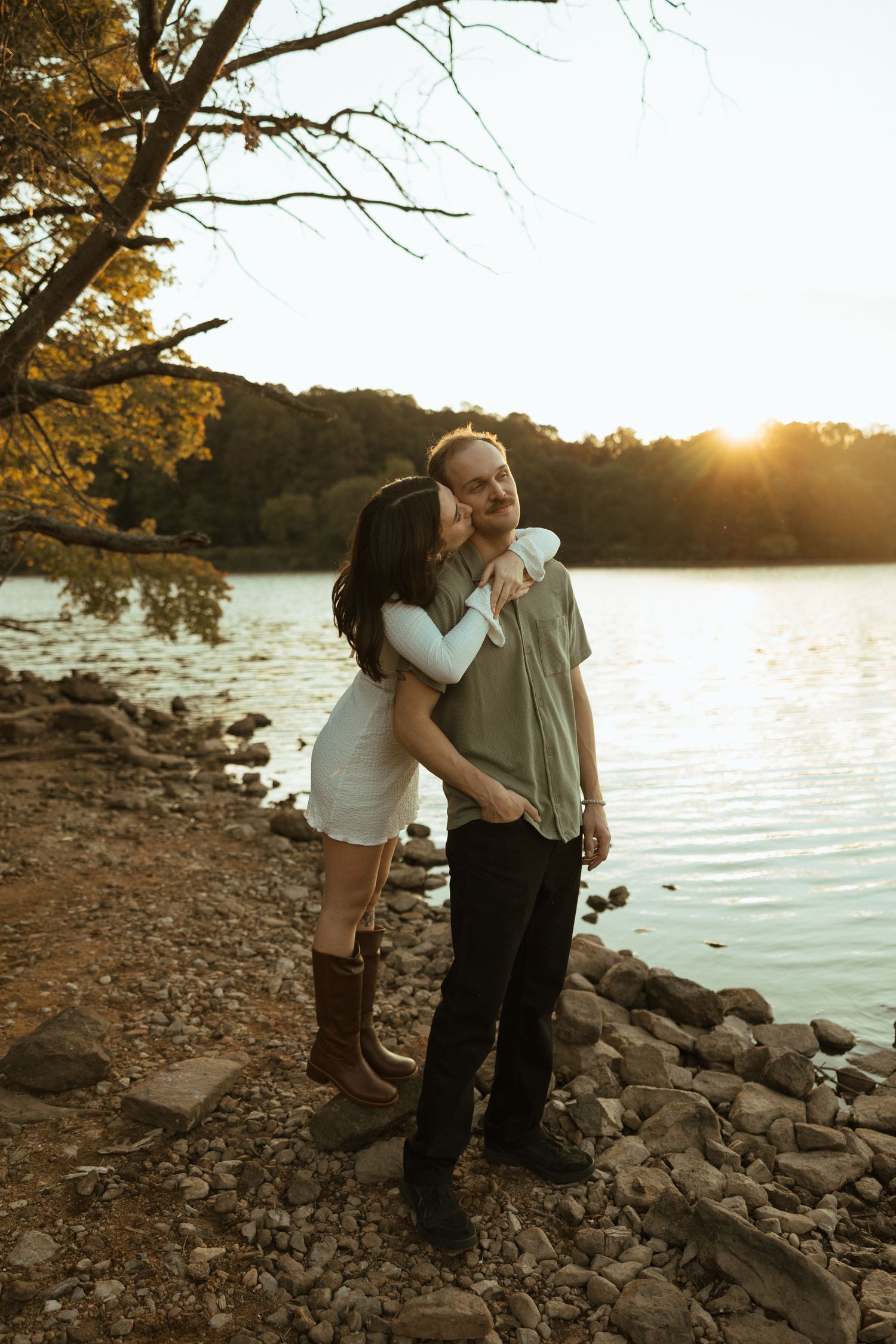 A couple shares an intimate moment at sunset by a rocky lakeshore.