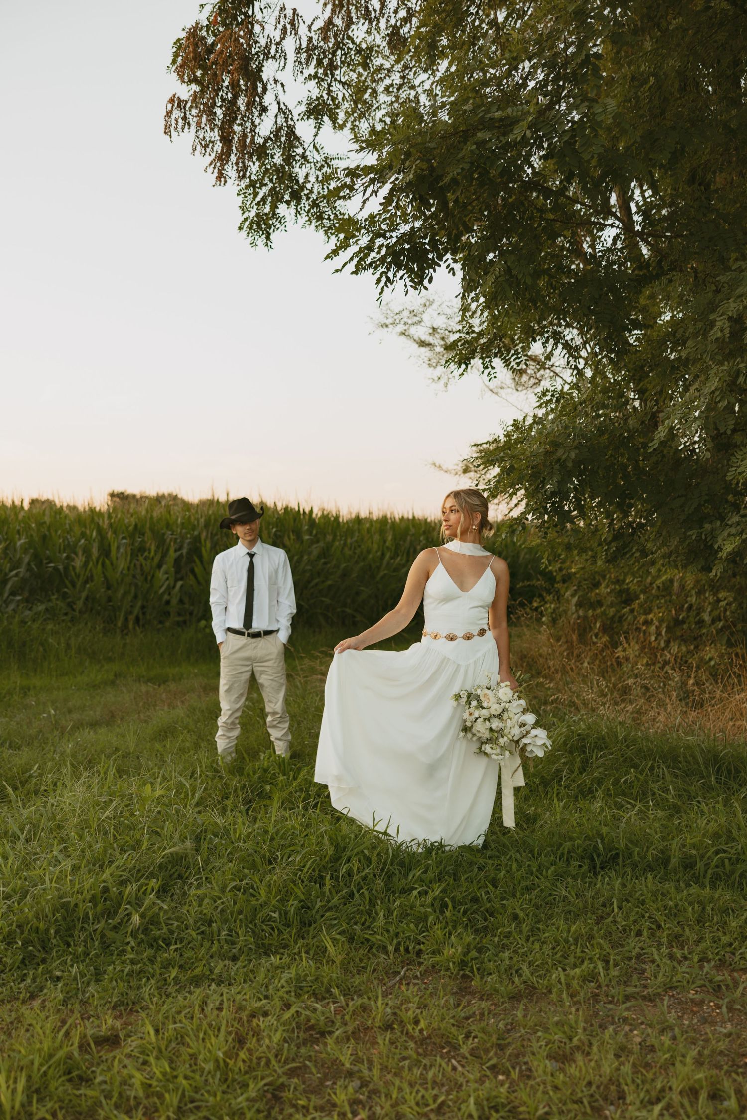Couple in white clothing playing with flowing dress fabric in a rural field at sunset.