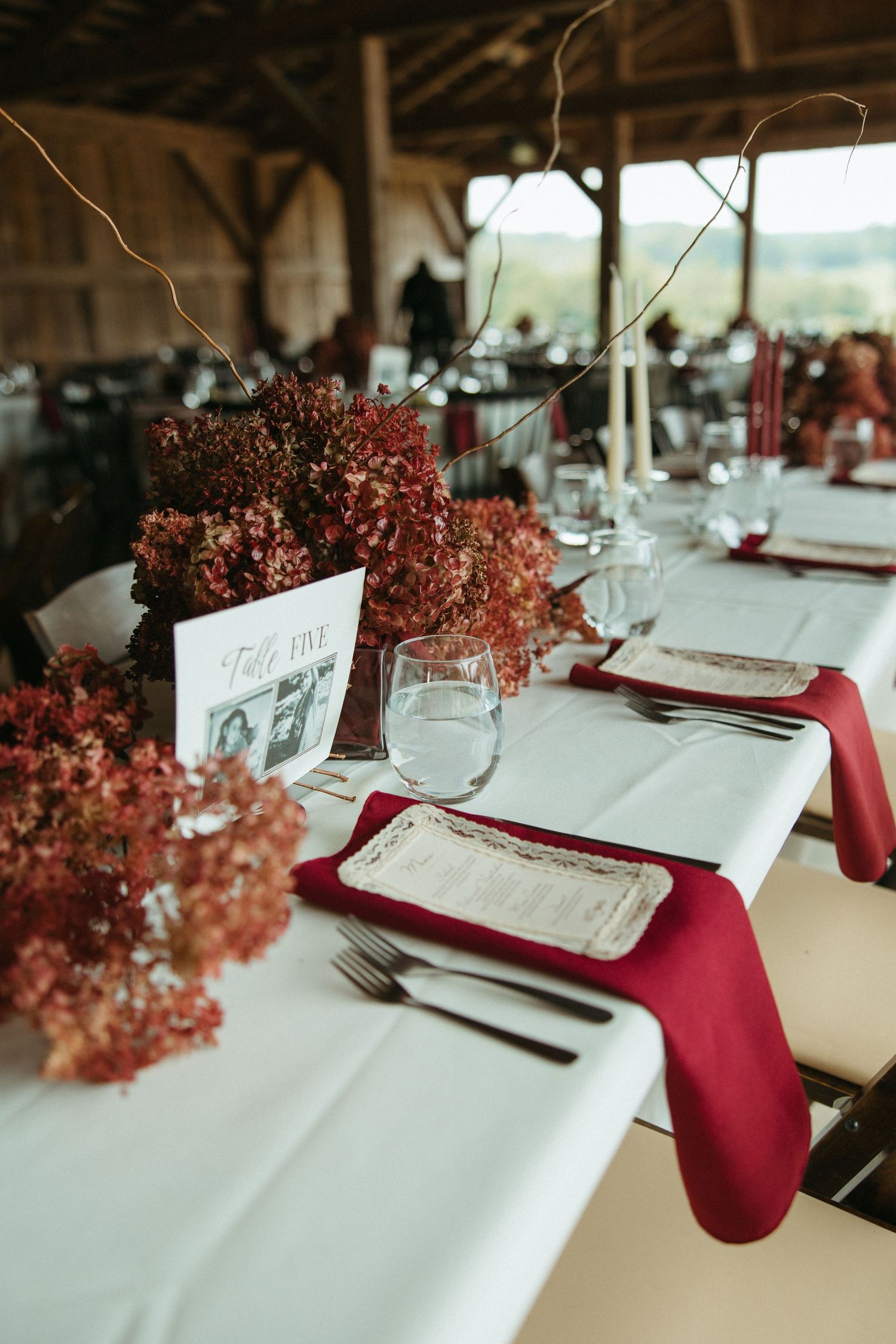 Elegant wedding table settings with burgundy napkins and pink floral centerpieces on crisp white tablecloths.