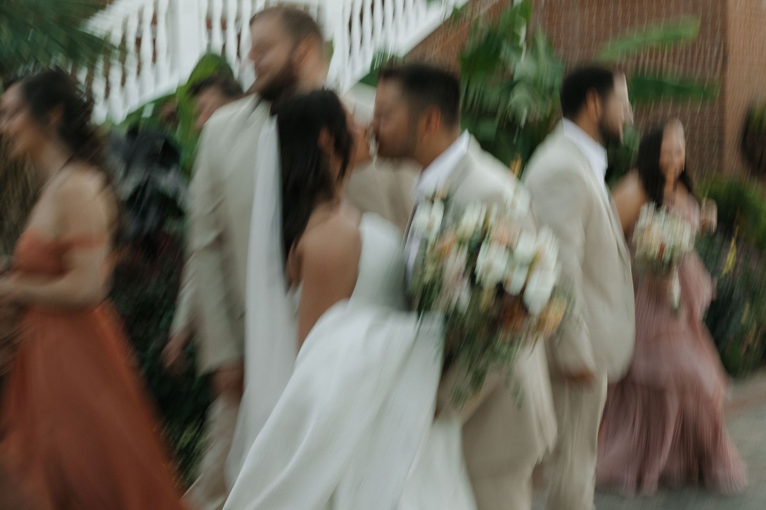 Wedding guests mingle and socialize at an outdoor garden reception venue with tropical greenery.