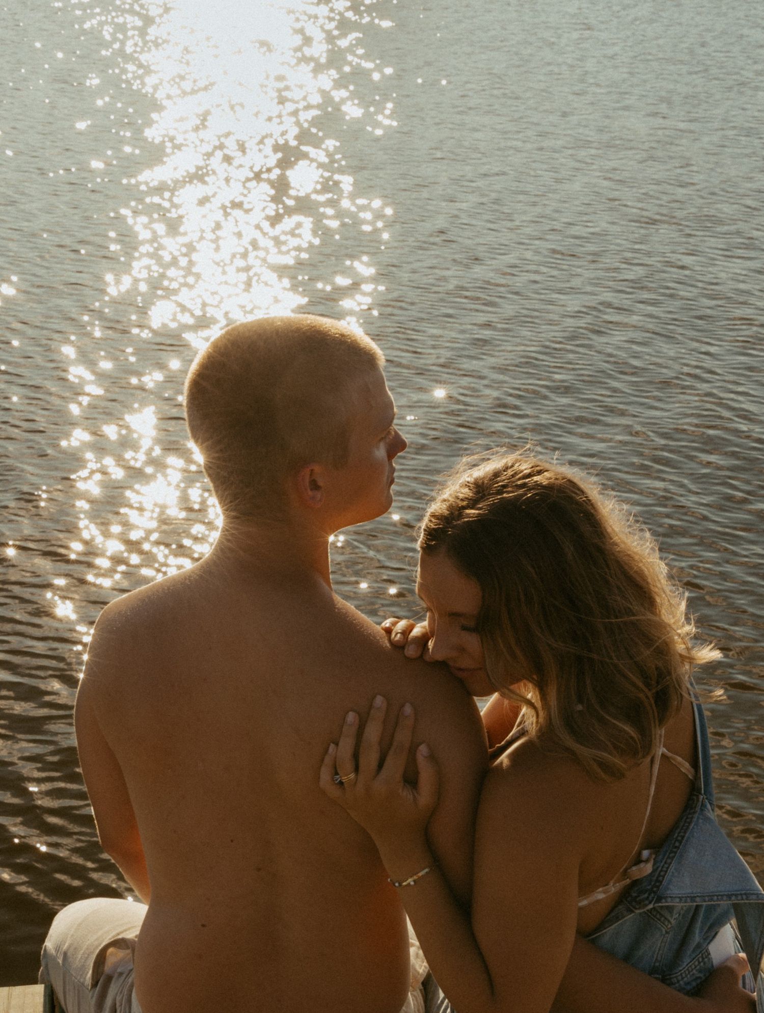 Romantic couple sharing an intimate moment by a sparkling lake at sunset.