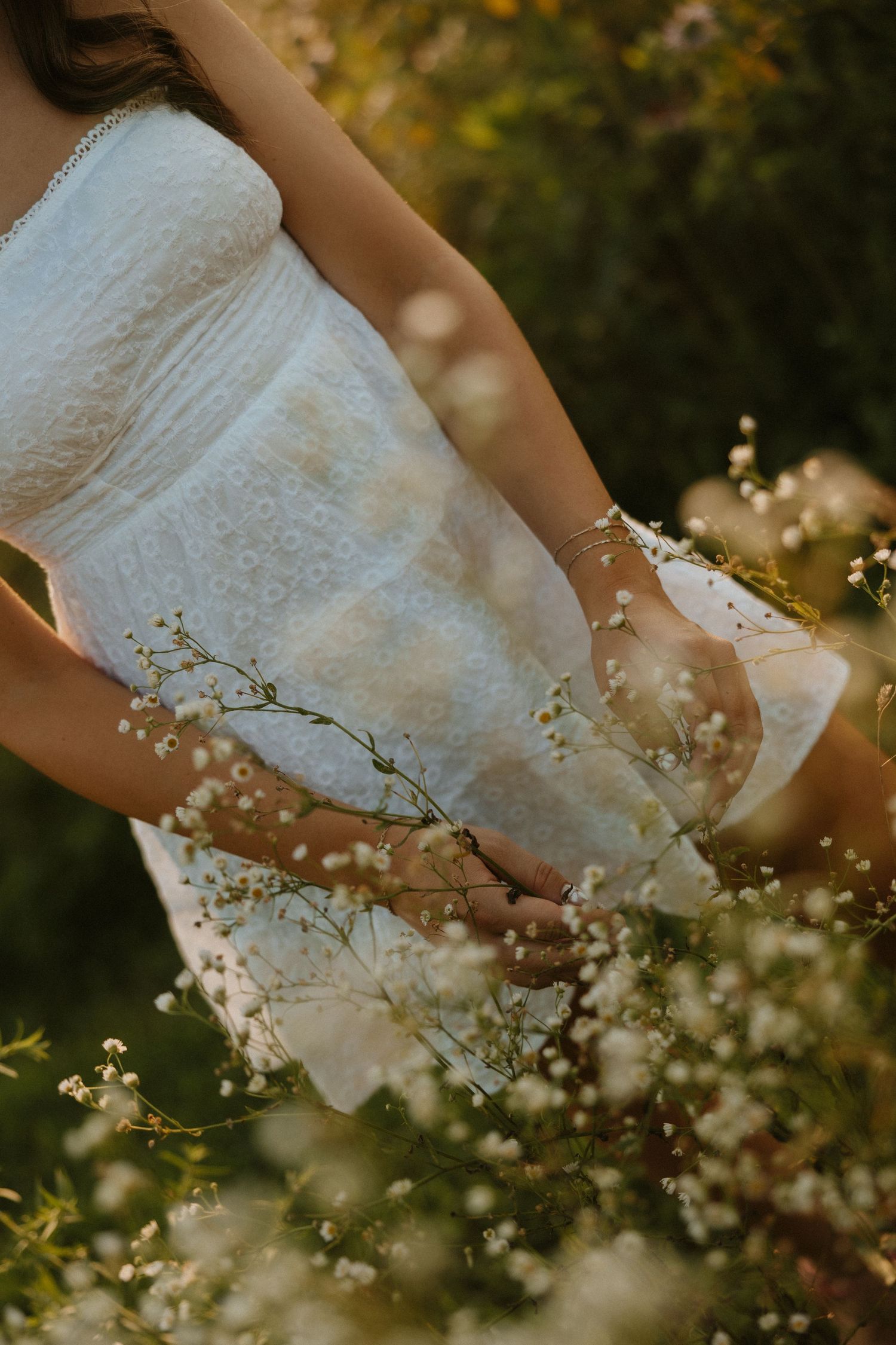 A white lace wedding dress flows gracefully among delicate white spring blossoms in a romantic garden setting.