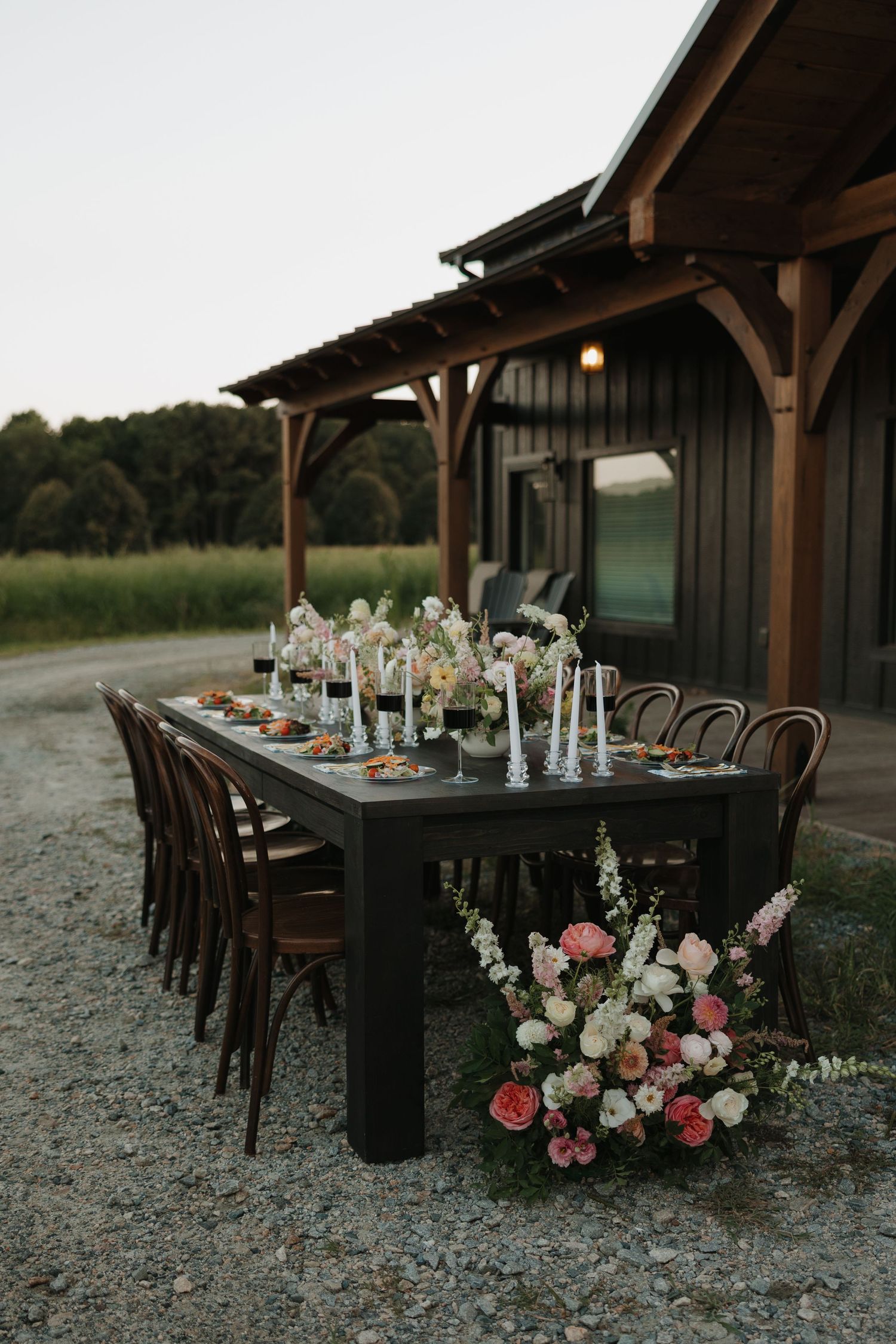 Elegant outdoor wedding reception table setup with black tablecloths and floral arrangements under a wooden pavilion.