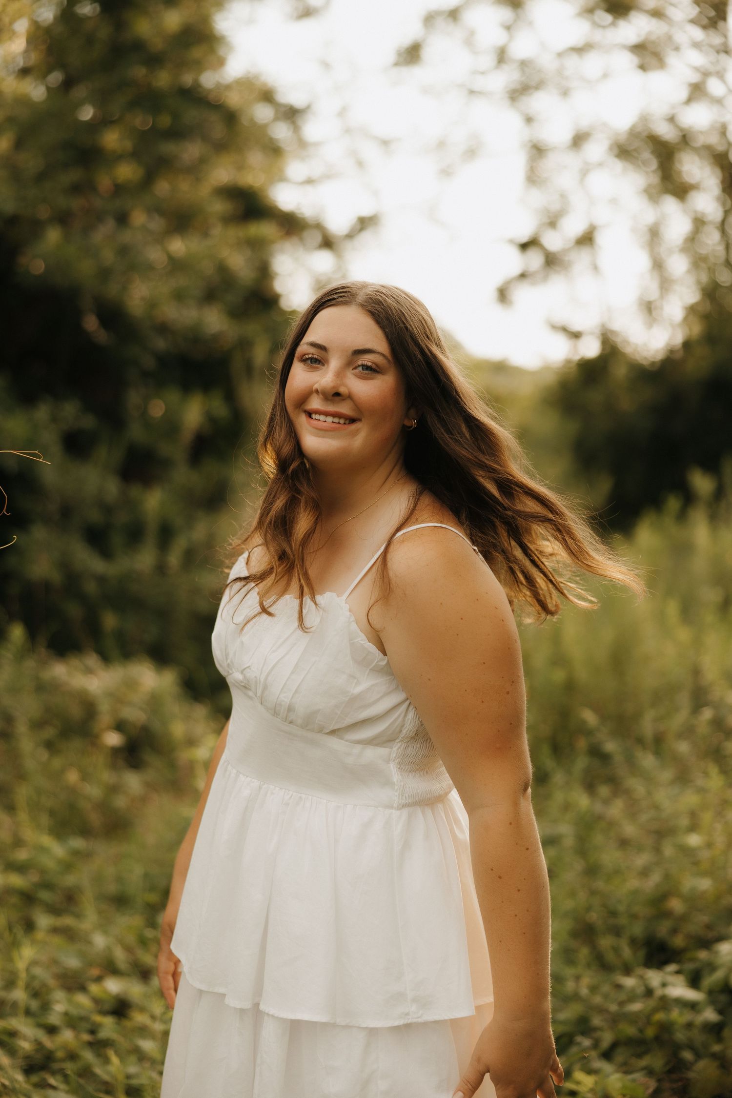 A person in a flowing white dress twirls joyfully in a sunlit meadow during golden hour.