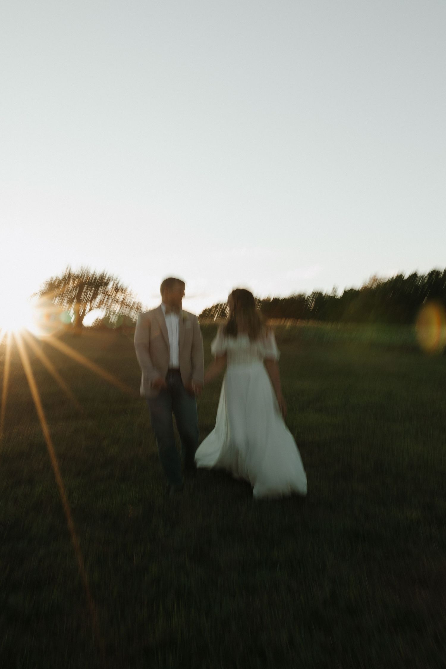 Silhouettes of a couple walking through a field at sunset with golden light streaming through the scene.