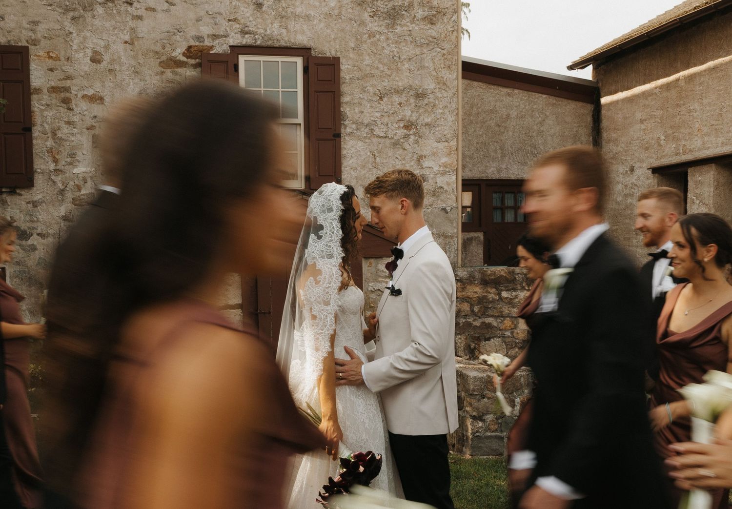Wedding reception guests dancing and celebrating in a rustic brick-walled venue with warm lighting.