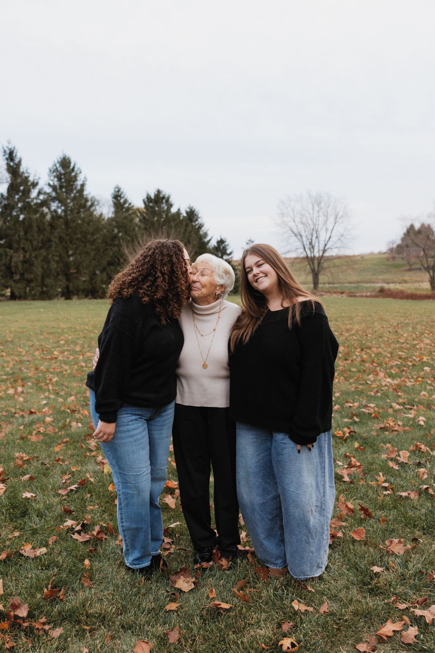 A group of friends in casual denim and sweaters huddle together on an autumn field with fallen leaves.