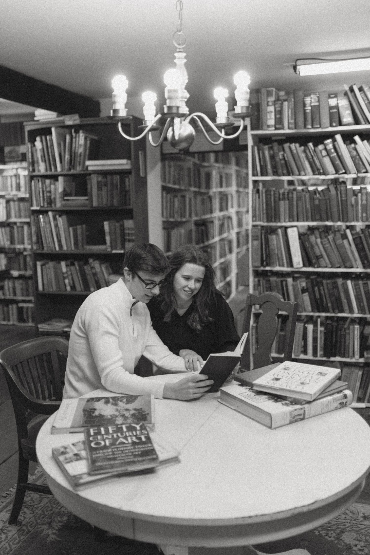 Students studying together at a round table in a library surrounded by bookshelves.