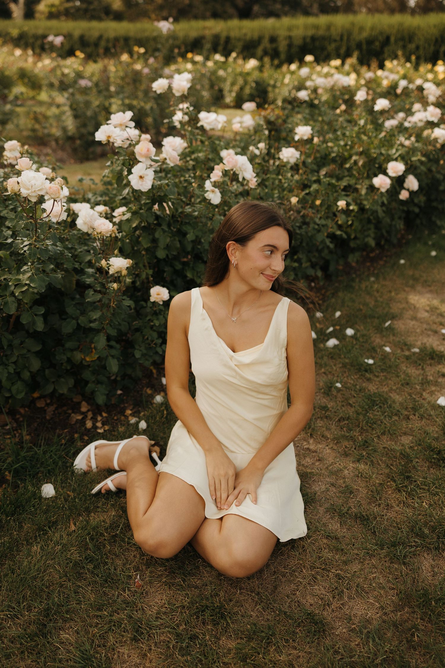 A dreamy portrait session in a garden with white roses and a flowing white dress creates a romantic summer atmosphere.