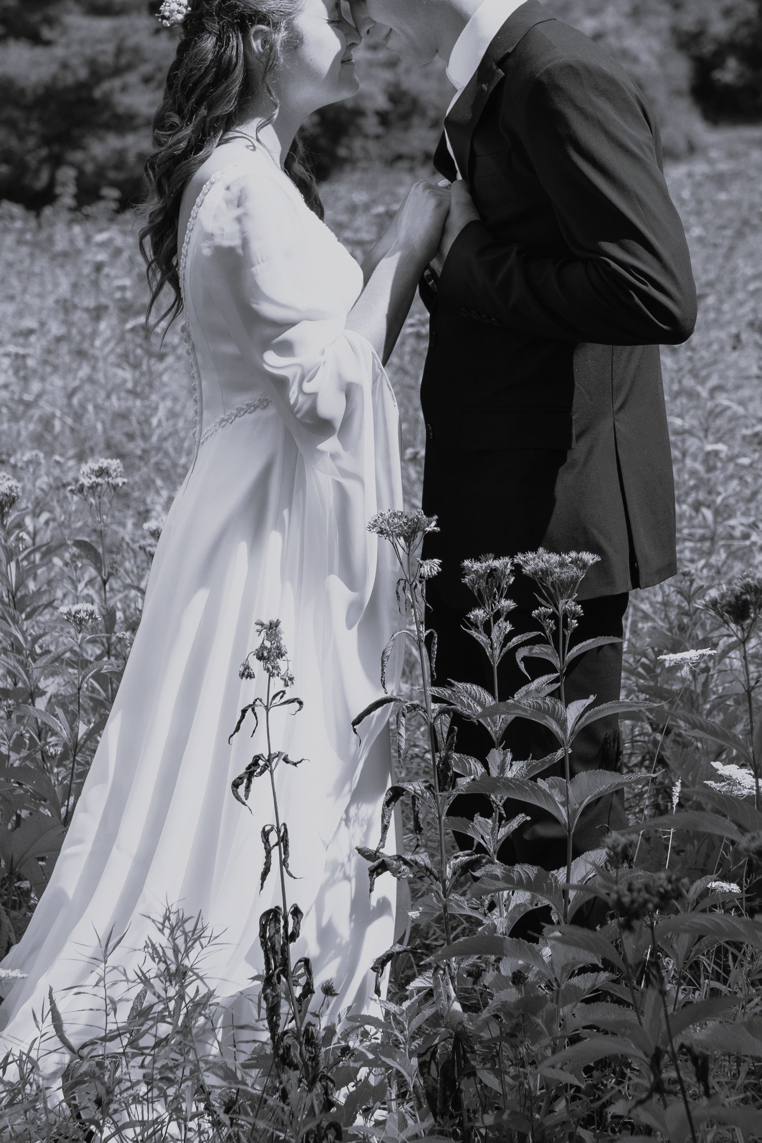 A romantic black and white photo of a couple in wedding attire standing among wildflowers.