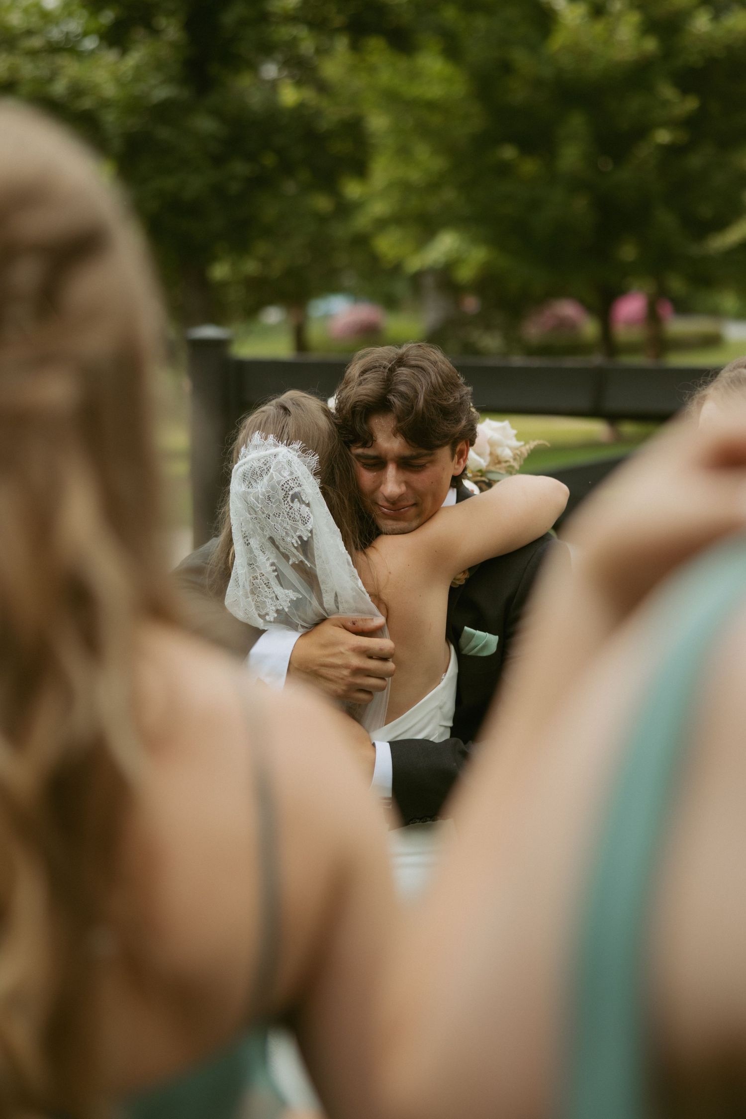 A couple shares an intimate embrace during an outdoor wedding ceremony, surrounded by greenery and soft lighting.