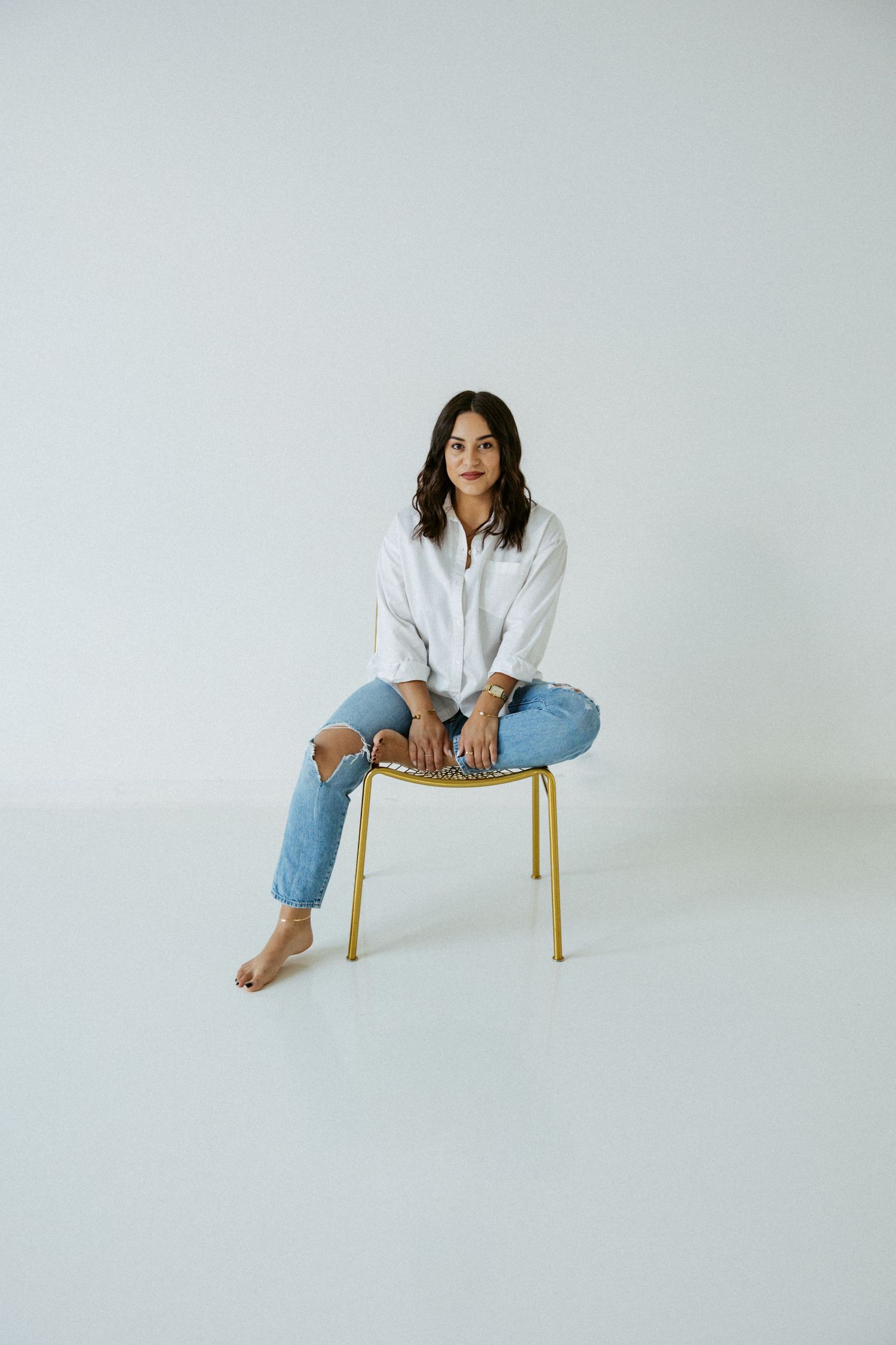 Minimalist portrait series of a woman in casual attire posing on a wooden chair against white background.