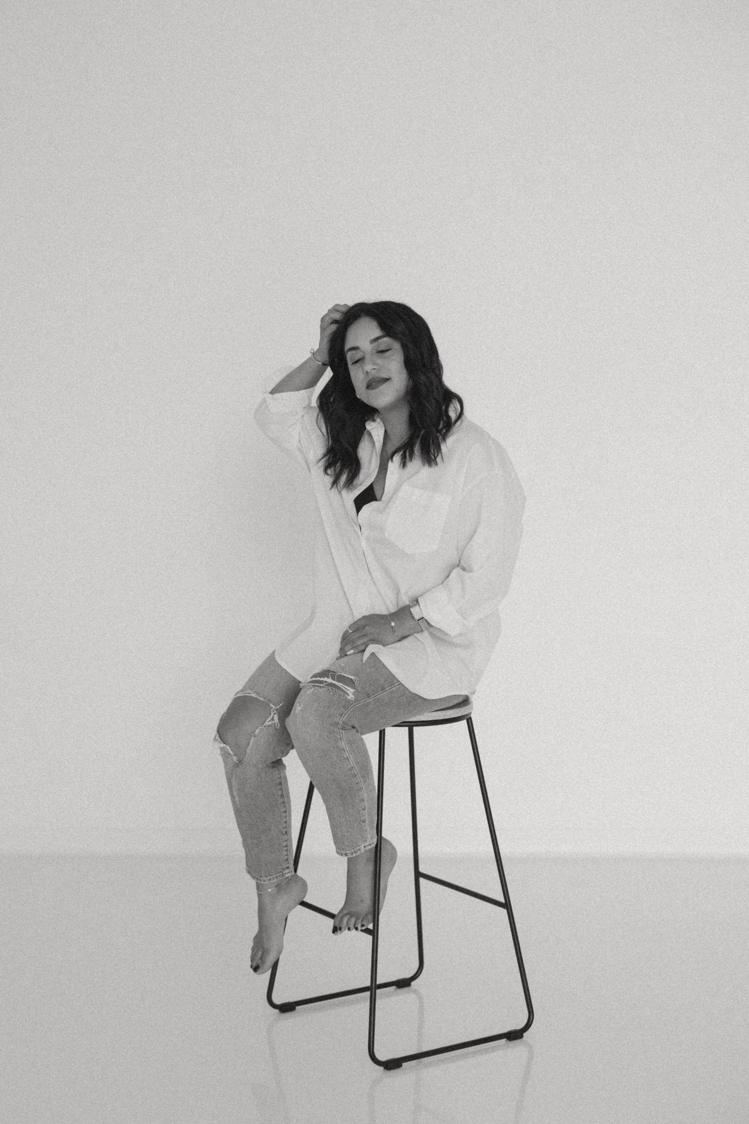 Artistic portrait series of a person in white shirt posing on a minimalist chair against white background.
