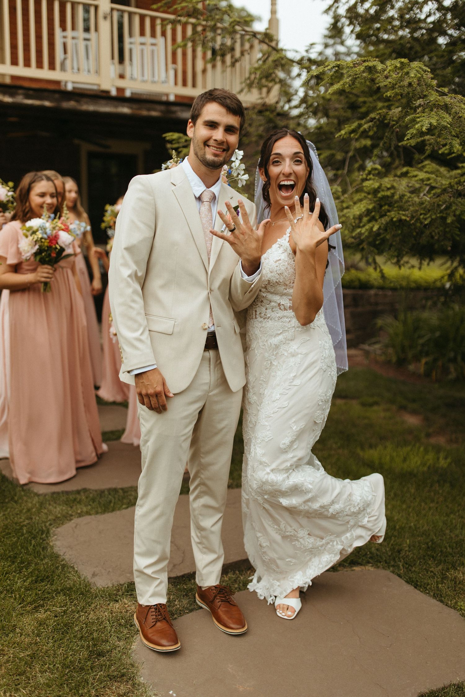 Wedding couple walks joyfully down a path together in coordinated white outfits and brown shoes.