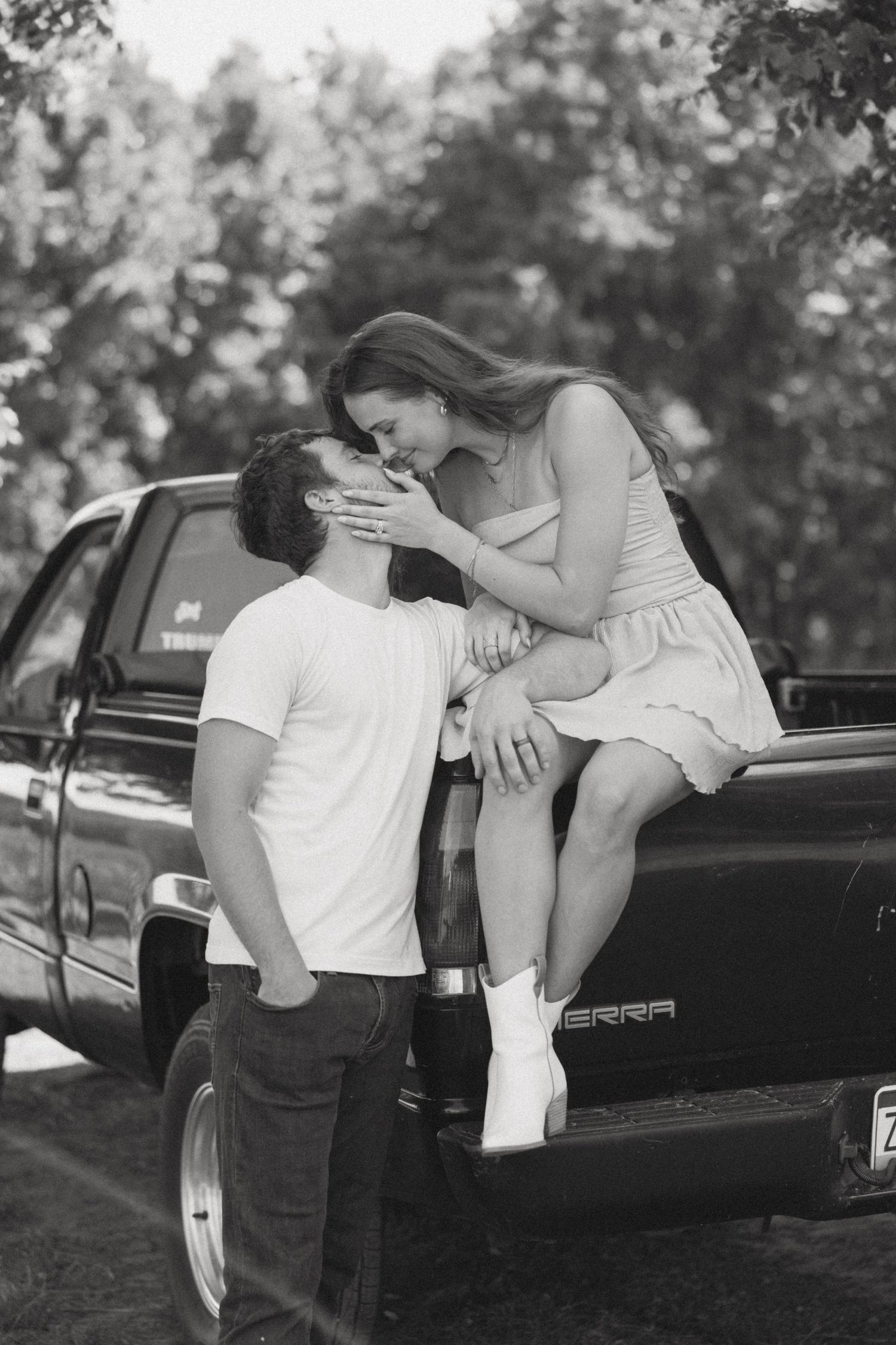 A romantic black and white photo of a couple sharing an intimate moment while sitting on a pickup truck.