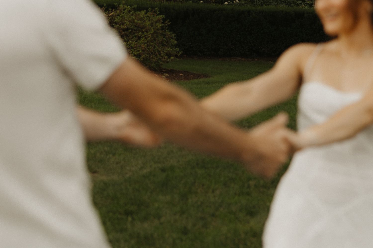 Newlyweds hold hands and walk through a lush garden setting during their outdoor wedding celebration.
