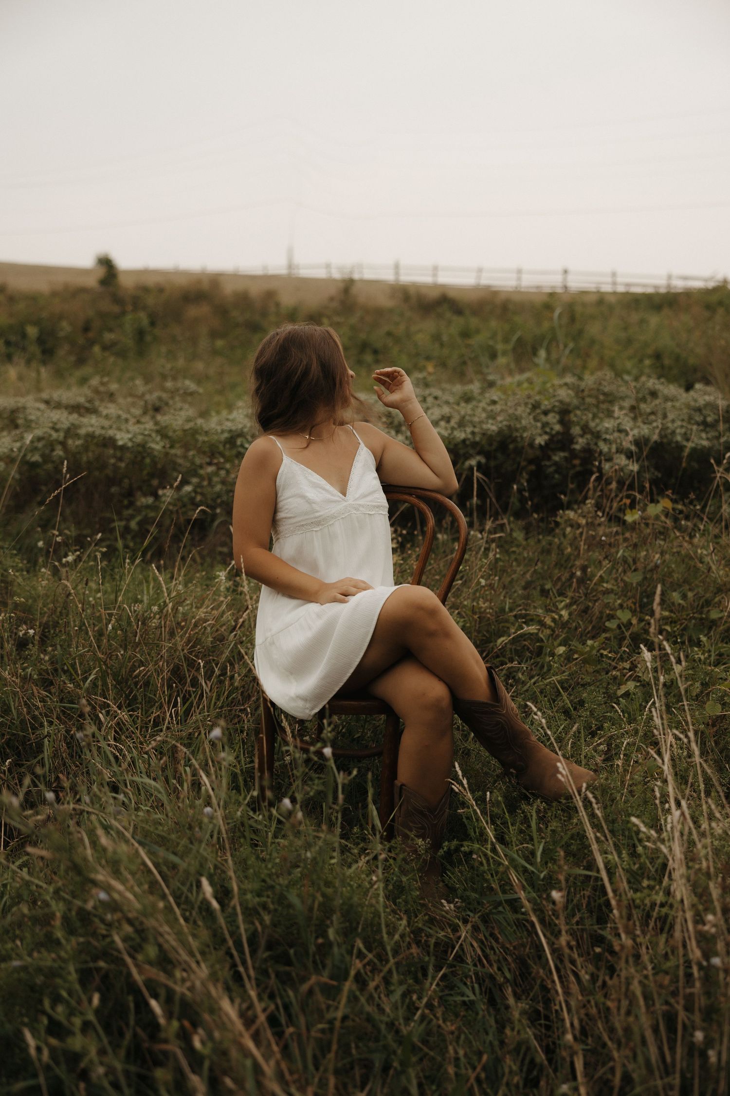 Person in white dress reclining on grassy hillside at golden hour.