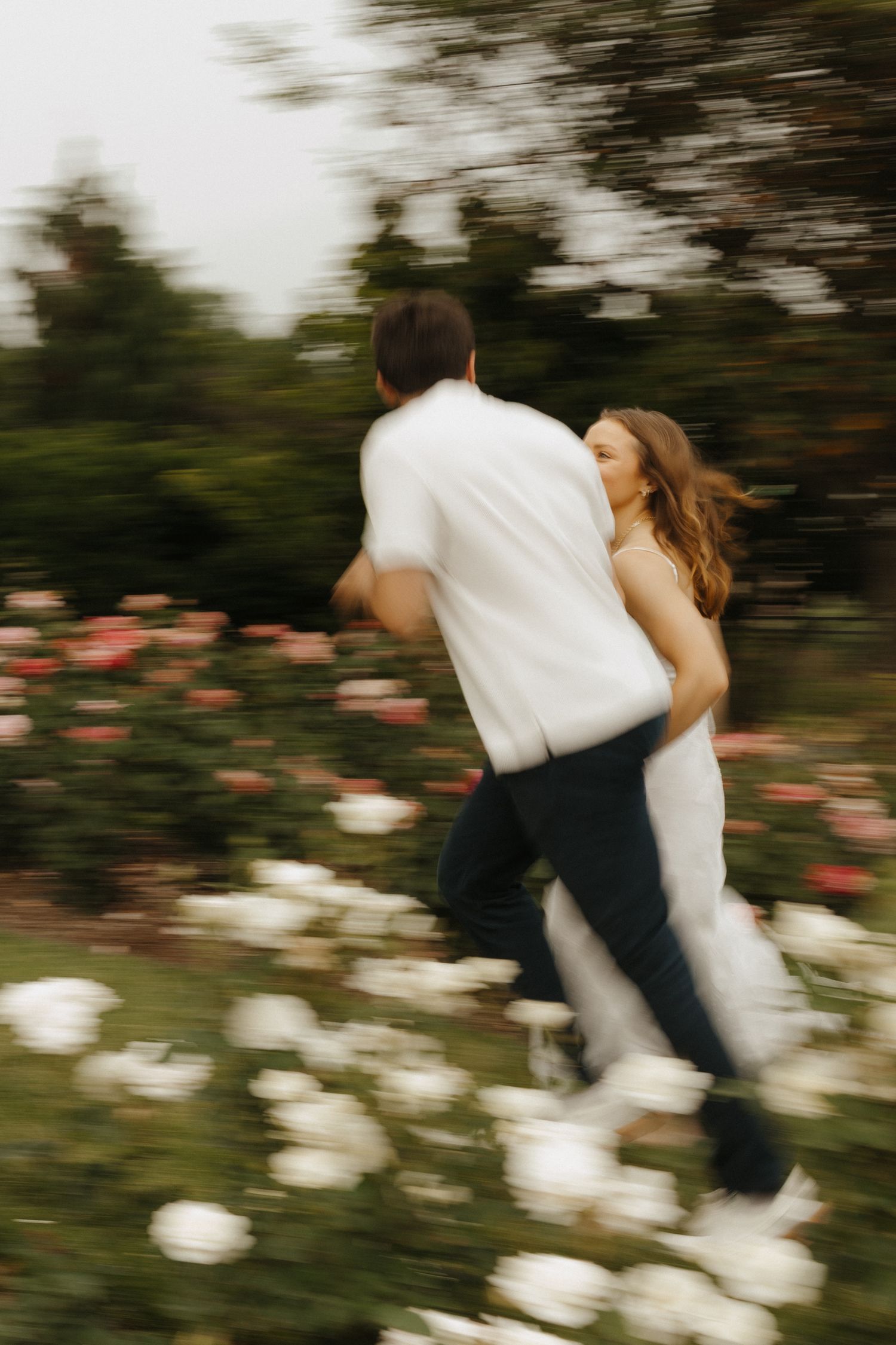 Motion-blurred photograph of a couple dancing and spinning in a rose garden at dusk.
