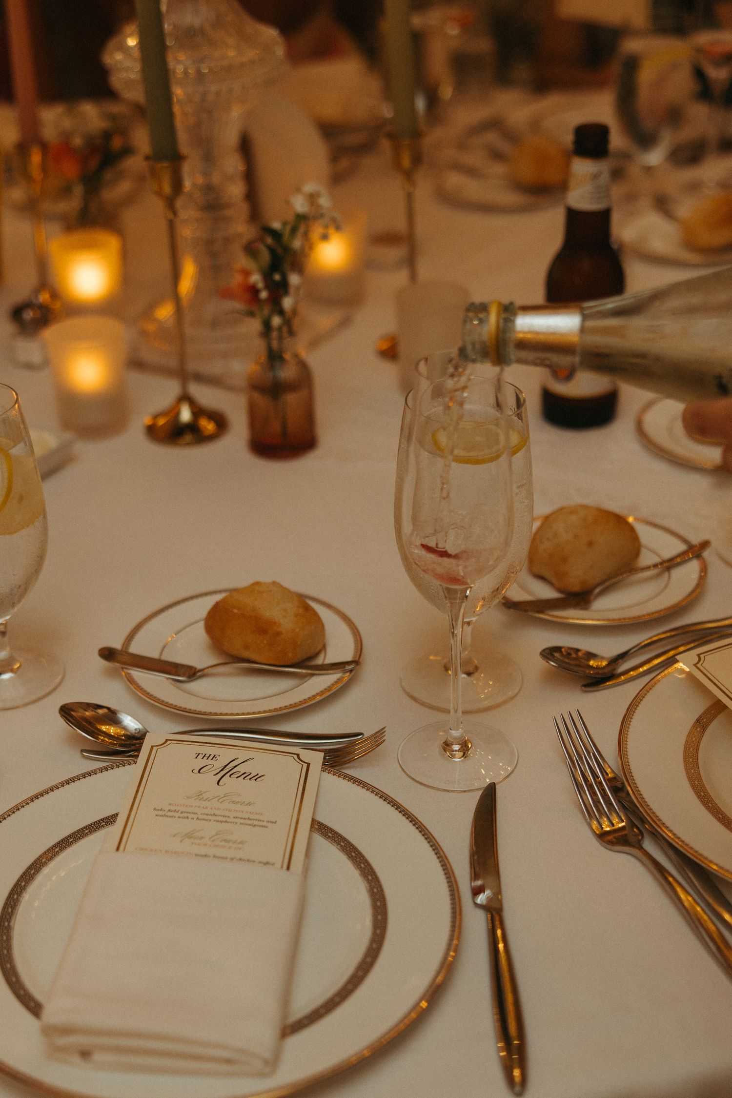 Elegant table setting at formal dinner with white linens, gold-rimmed plates, and glowing candlelight.