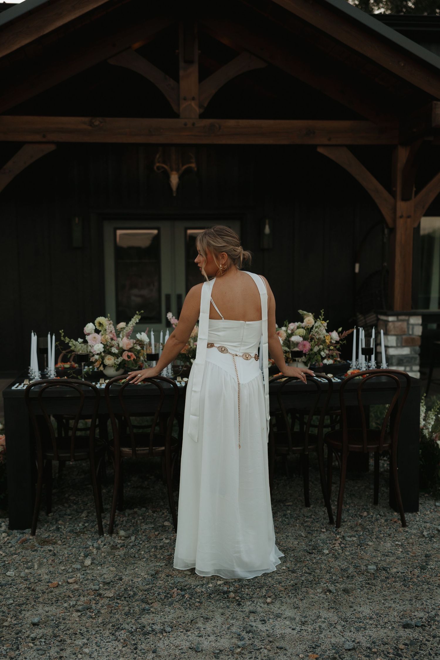 Back view of person in flowing white dress walking through rustic outdoor venue.