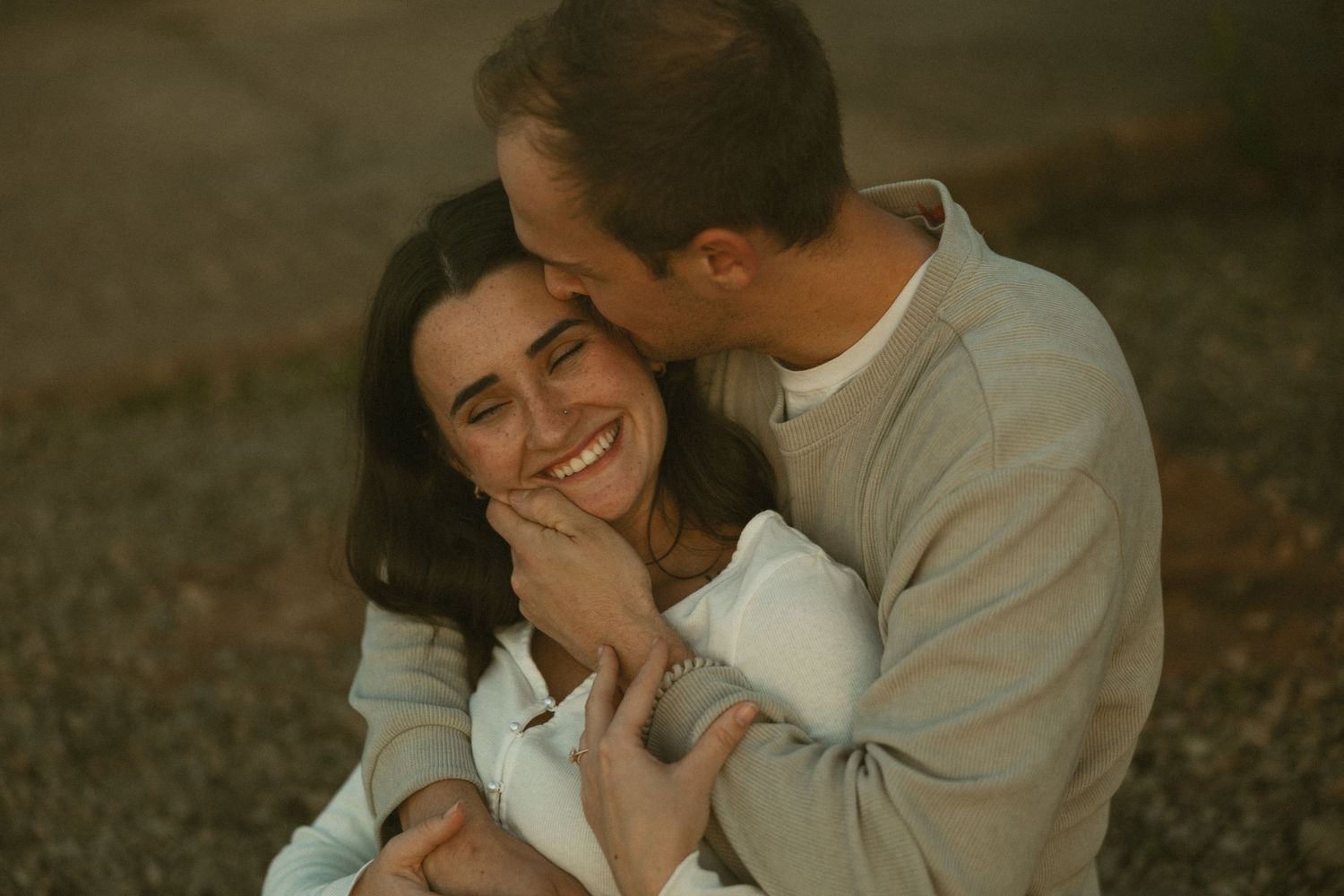 A couple shares intimate laughter while sitting together outdoors during a romantic photoshoot.