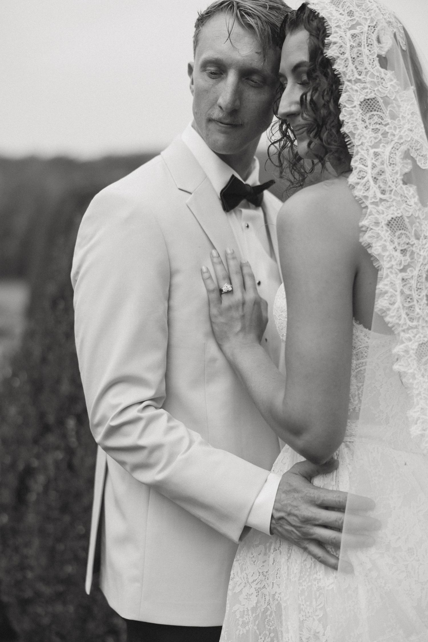 Black and white portrait of a romantic couple embracing in formal wedding attire.