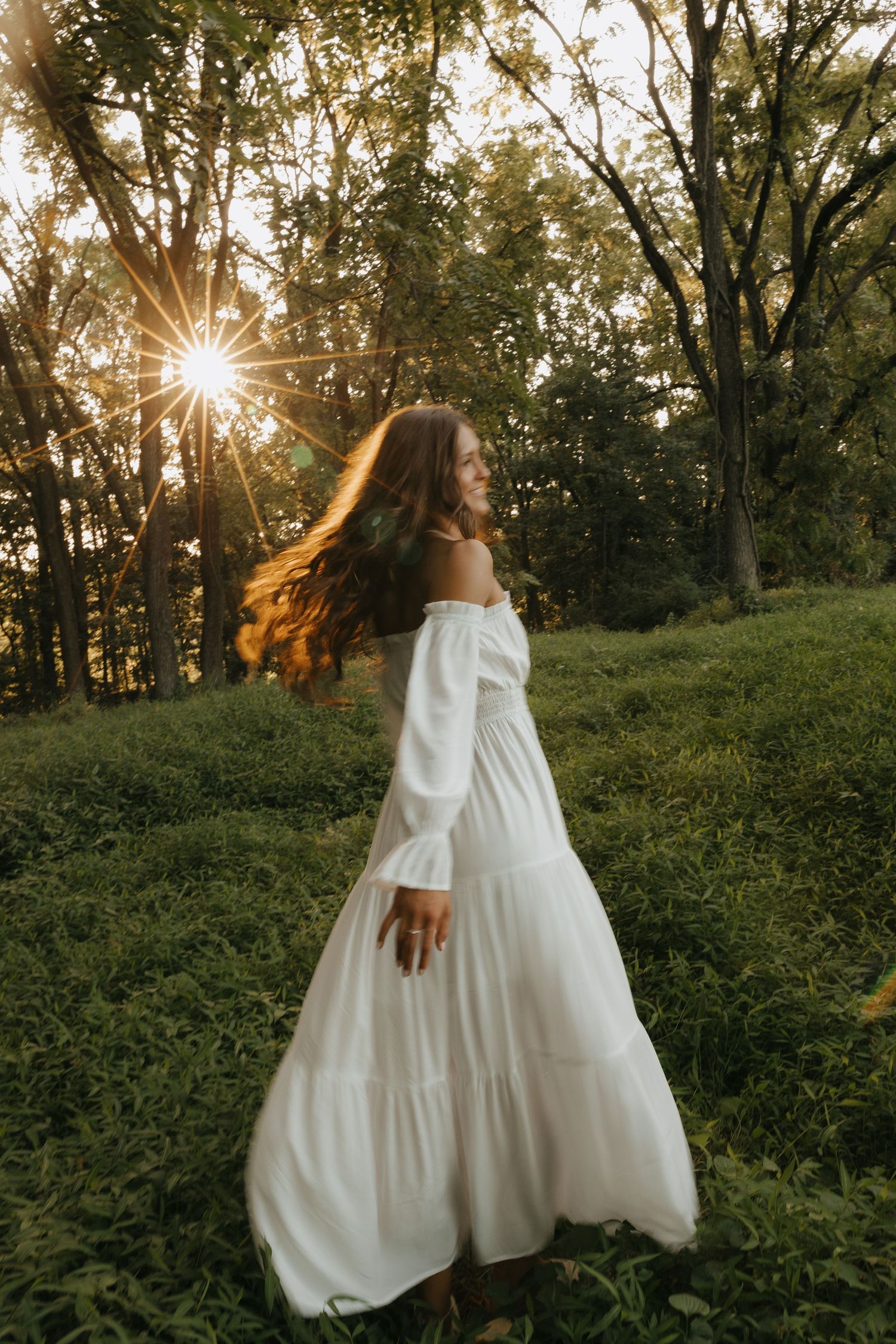 A person in a flowing white dress walks through a sunlit forest during golden hour creating an ethereal scene.