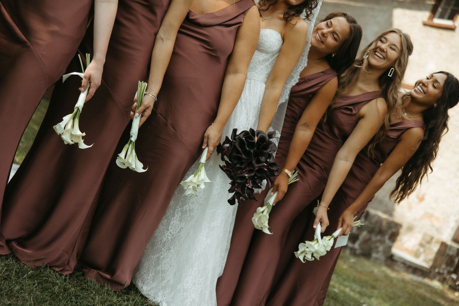 Wedding party in brown dresses and white gowns pose together in a garden setting.