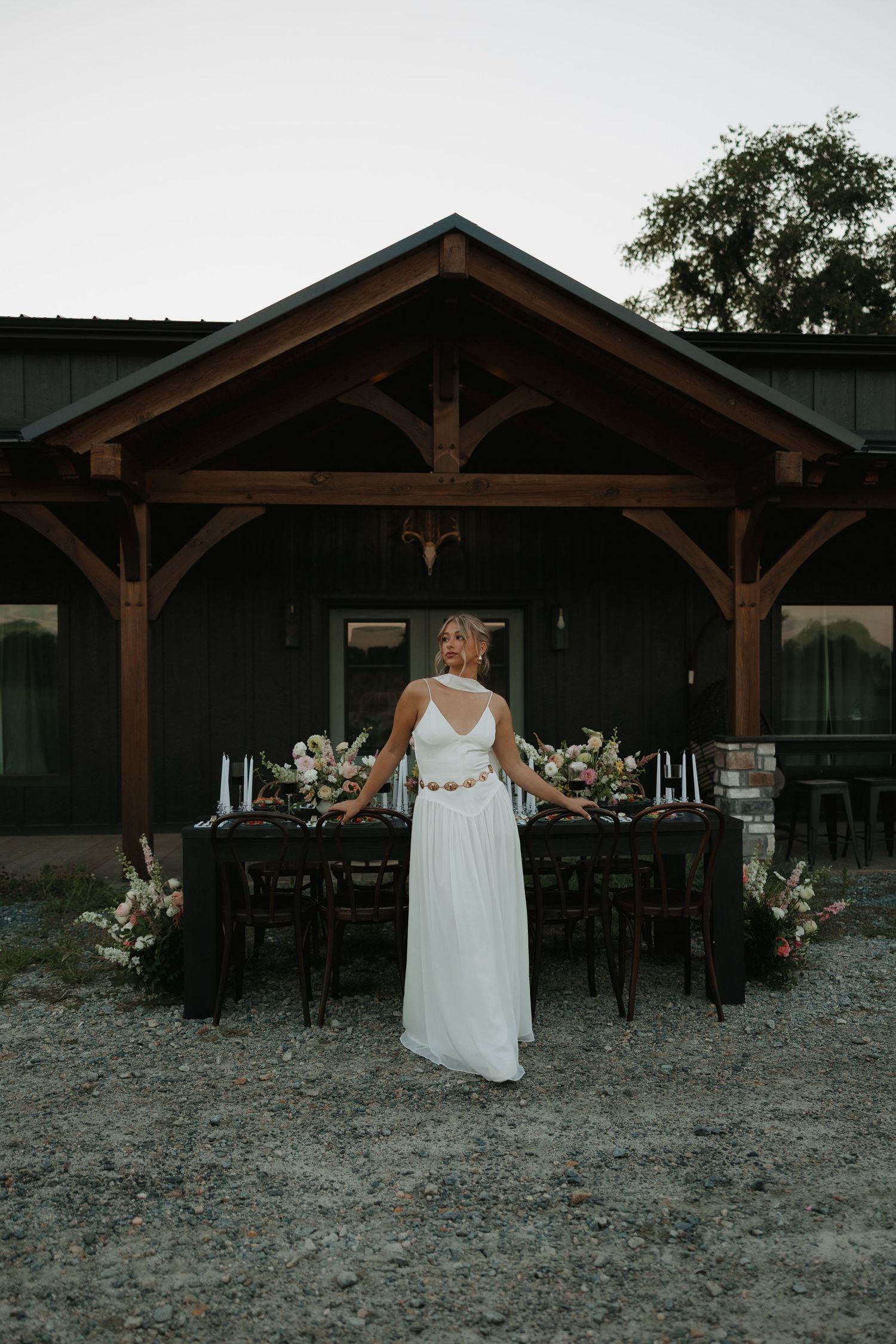 A rustic wooden pavilion with dark stained timber beams and posts stands in a gravel-covered outdoor event space.