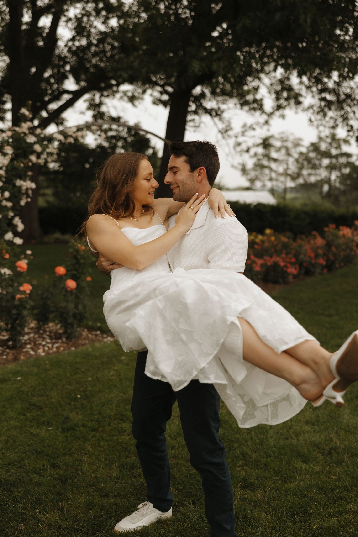 Playful couple spinning and dancing in a garden with orange flowers.