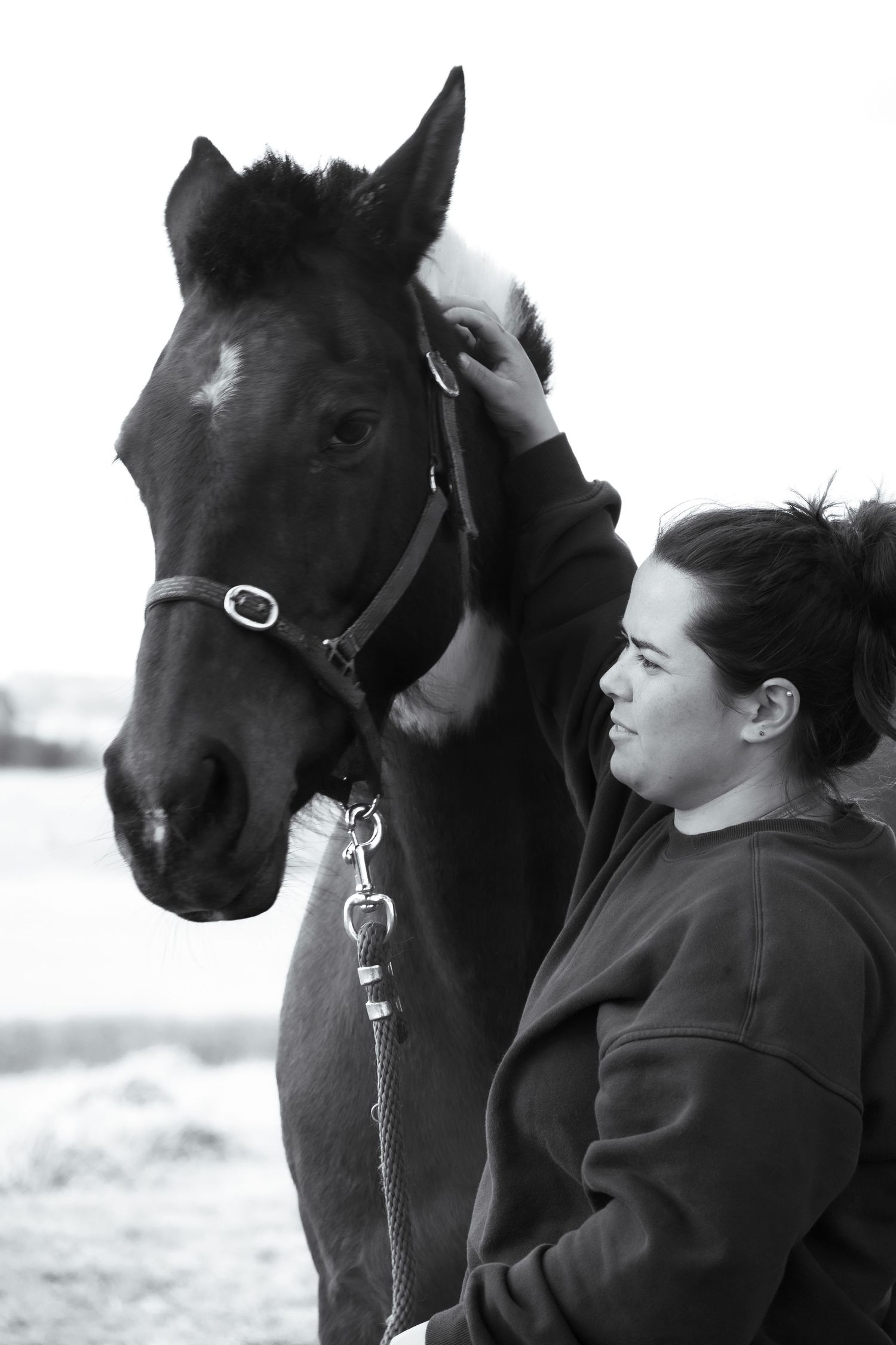 A black and white photo shows a person in dark clothing standing next to a dark-colored horse in a winter setting.