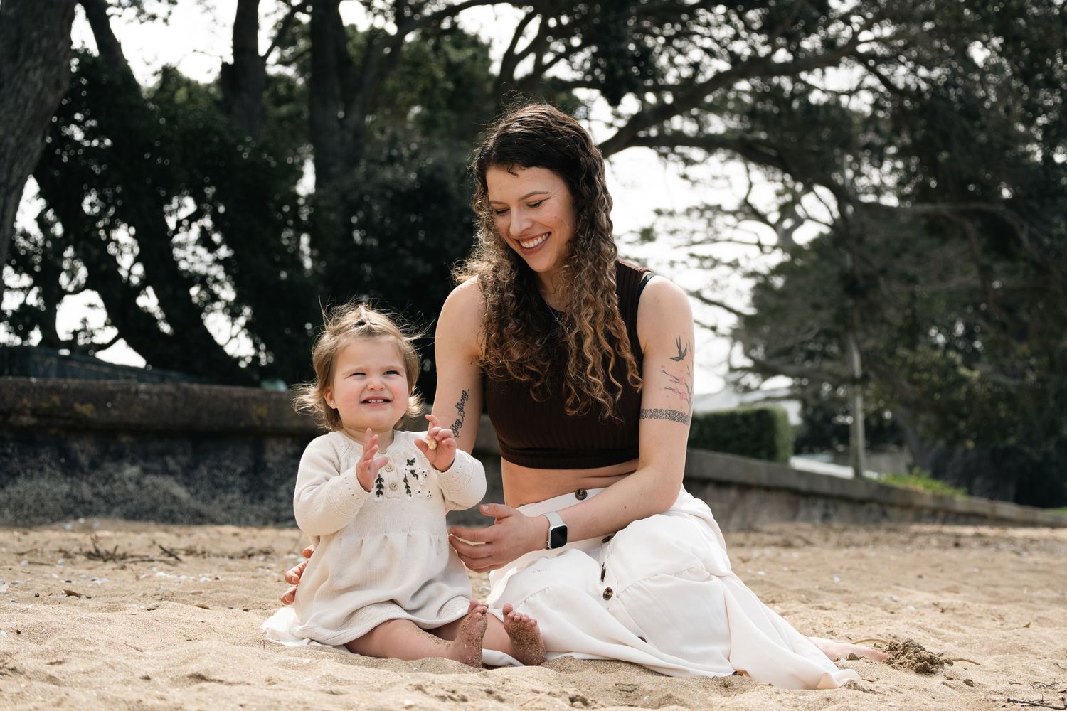 A family wearing white outfits sits together on a sandy beach during a casual outdoor photo session.