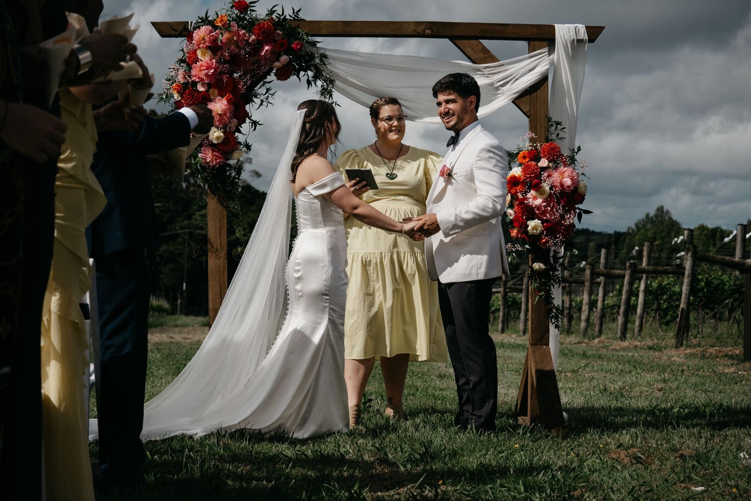 Wedding couple dances together at outdoor vineyard venue with red floral arrangements and stormy sky overhead.