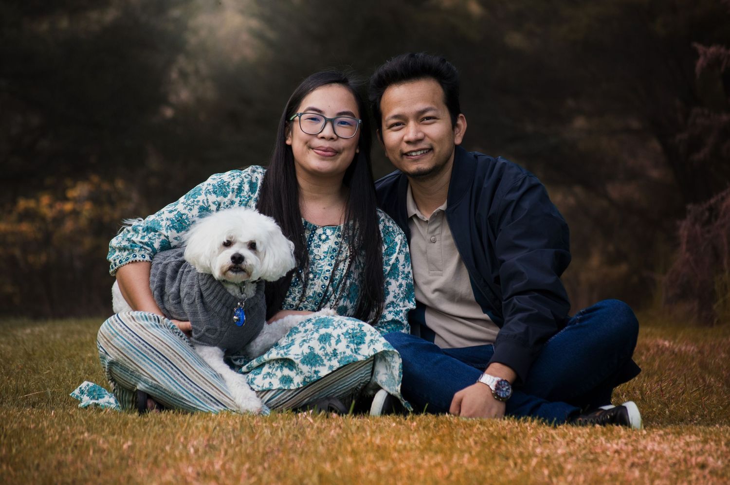 Couple sitting together outdoors with their white fluffy dog on a sunny autumn day.