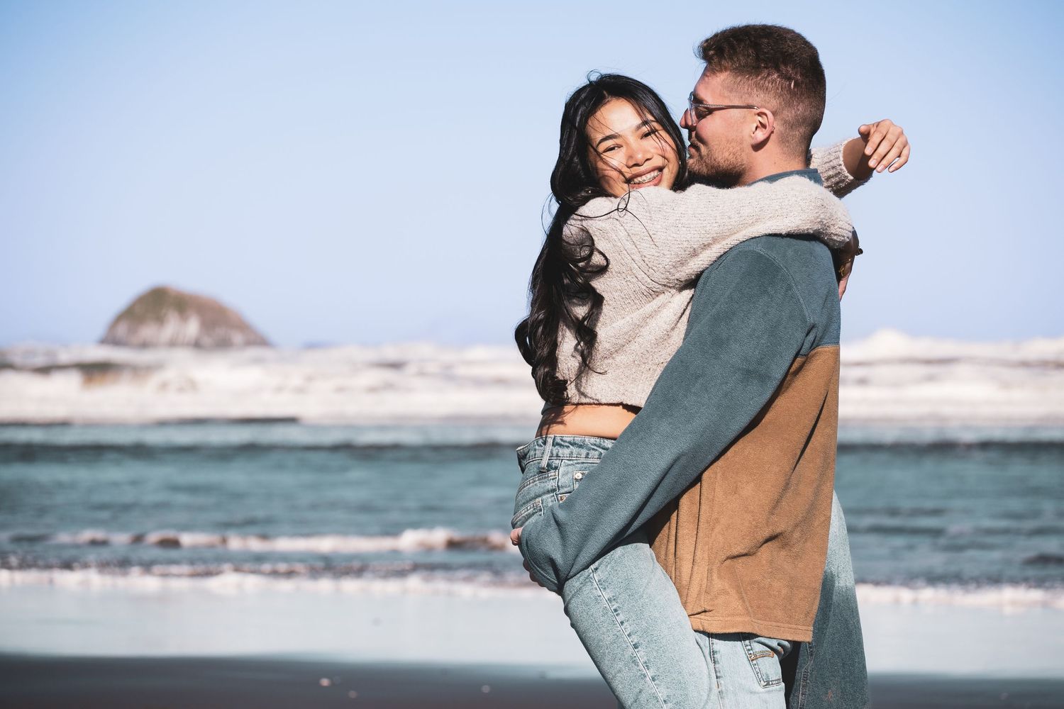 Couple embracing on a beach with white cliffs and ocean waves in the background during sunset.