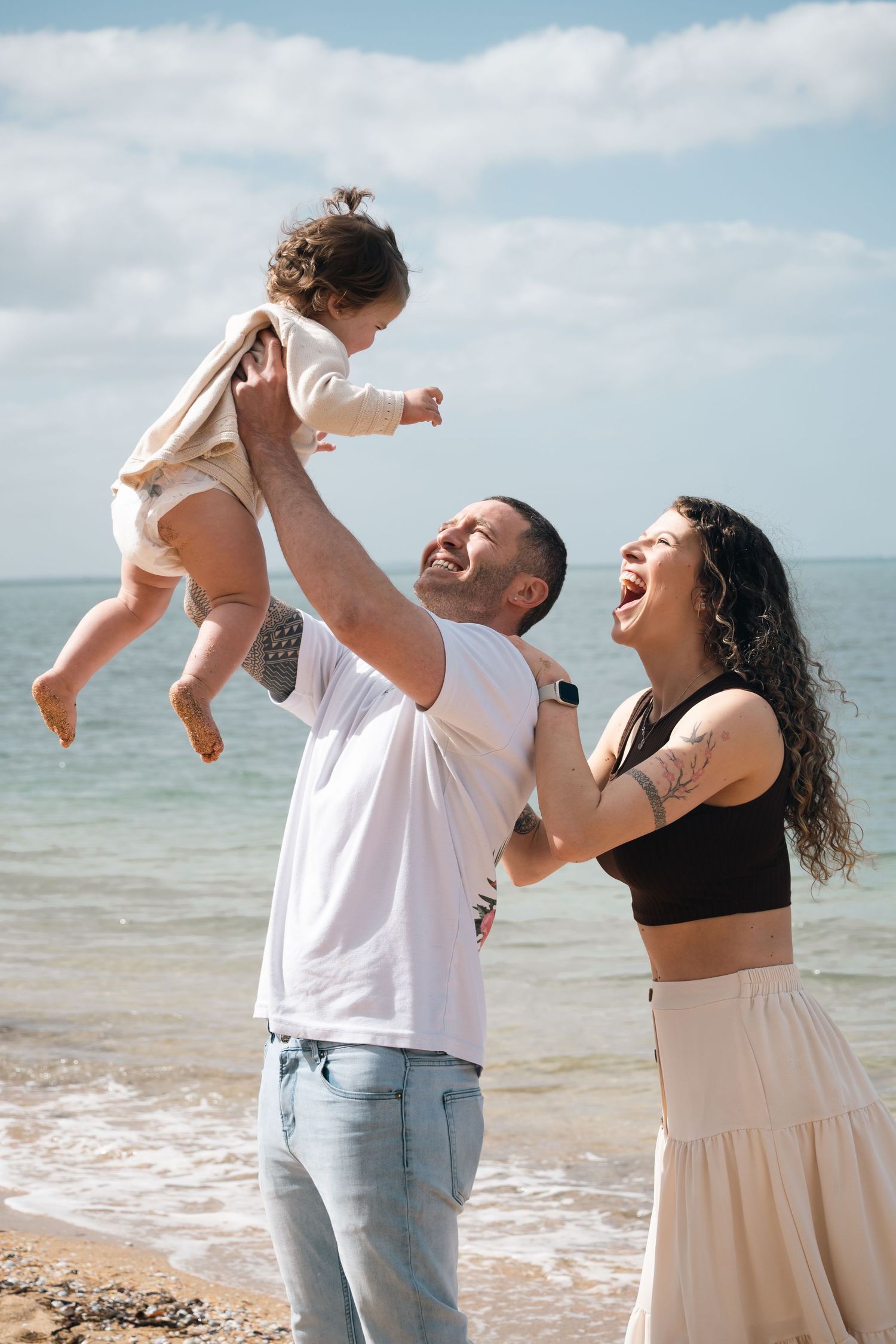 Family enjoying playful moments together at a sunny beach with waves in the background.