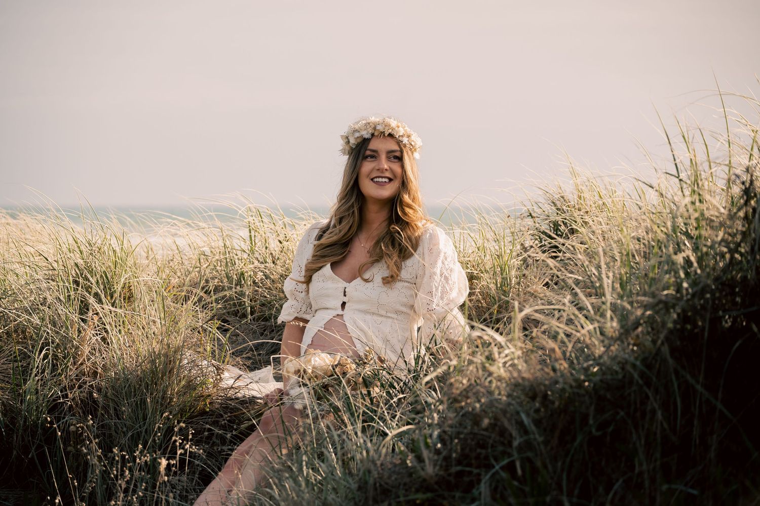 A person in a flowy dress stands among tall grass during golden hour at sunset.