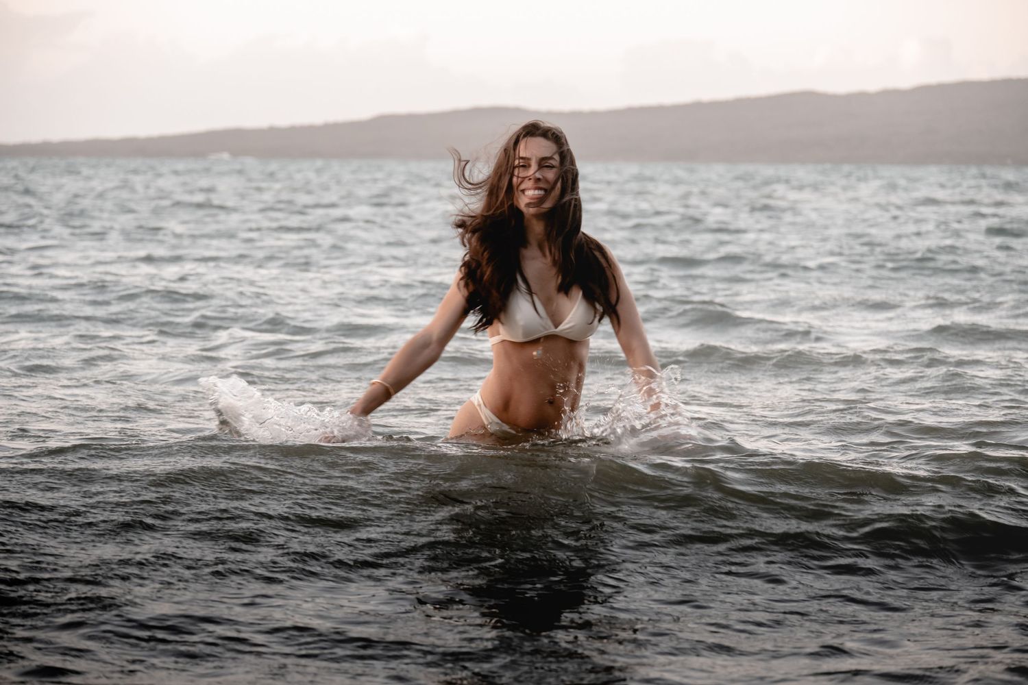 A person in a white dress floats gracefully in dark ocean waters at sunset creating a dreamy ethereal scene.