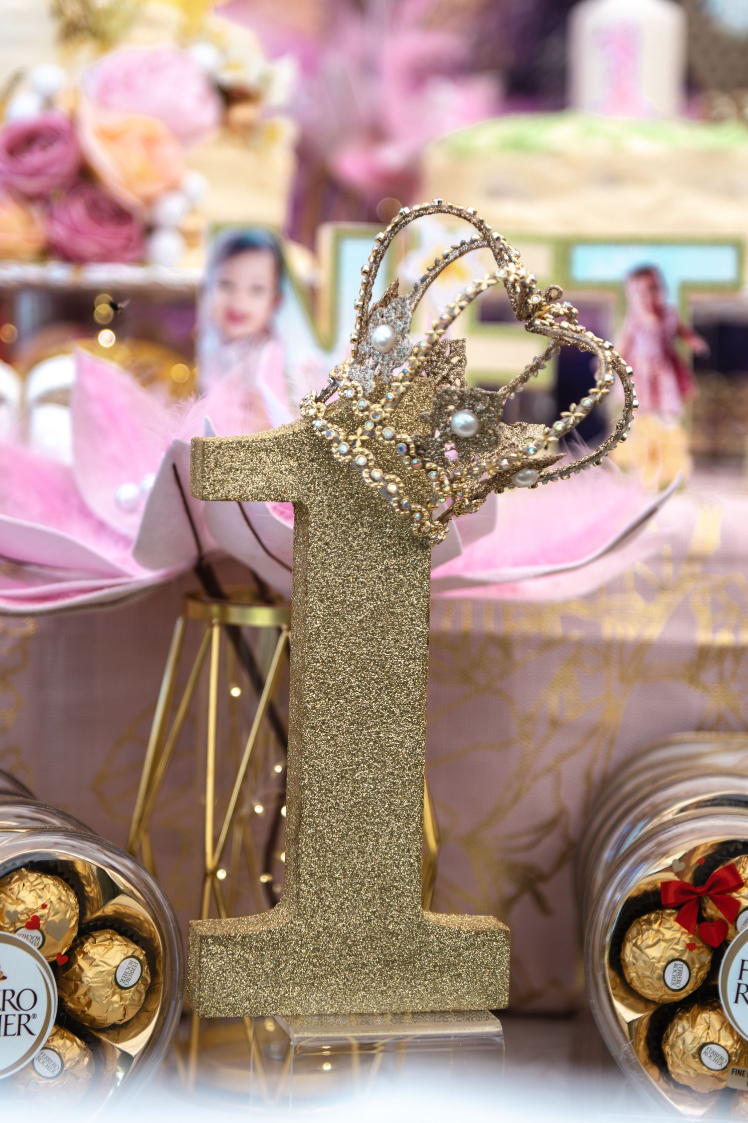 Gold glitter number one with crown decoration at a first birthday party, surrounded by Ferrero Rocher chocolates.
