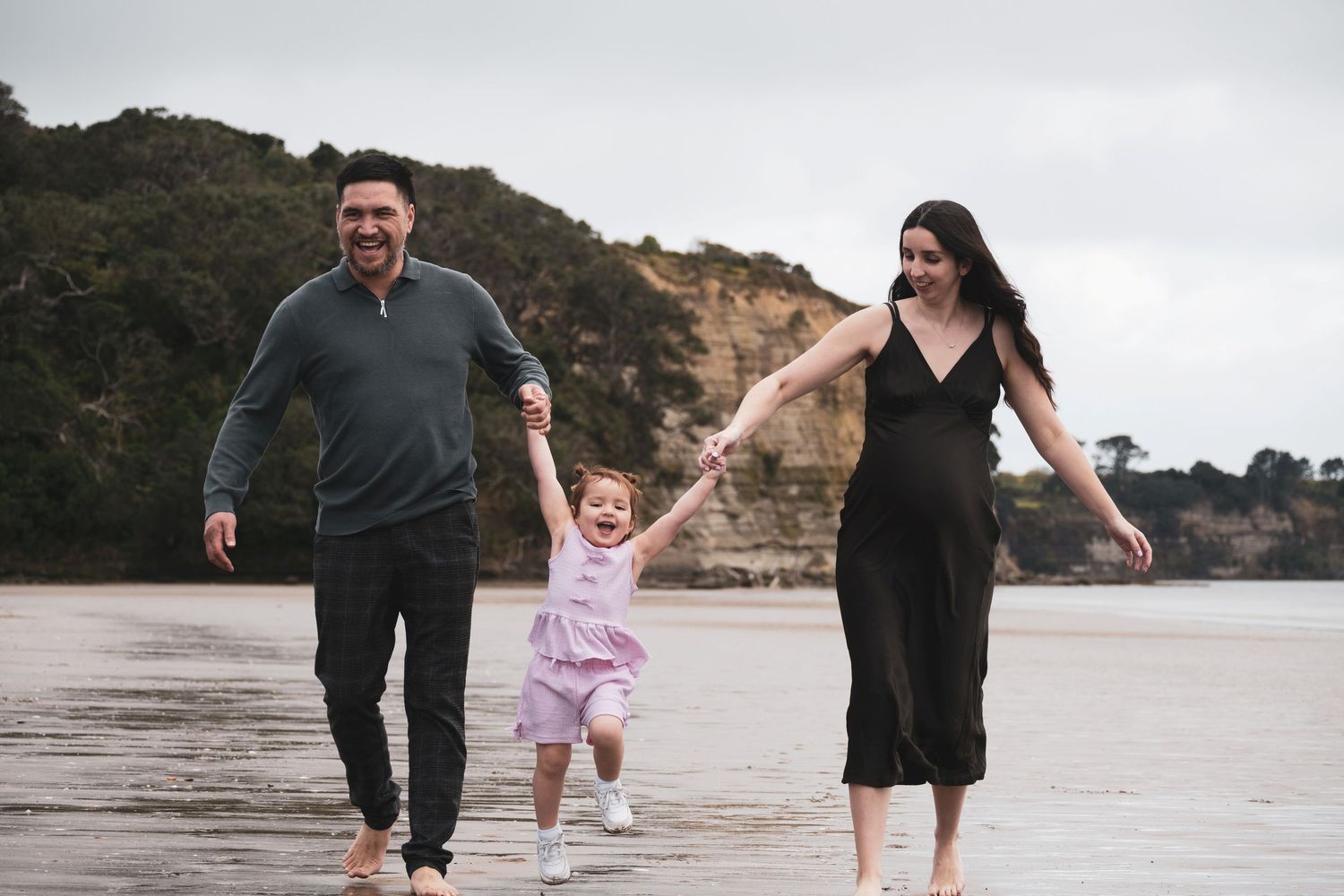 Family walking and playing together on a scenic beach with cliffs in the background during sunset.