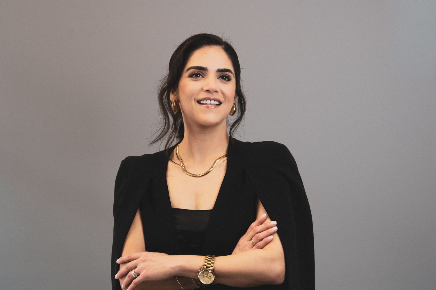 A person in a black outfit and gold jewelry smiles while posing for a photoshoot series.