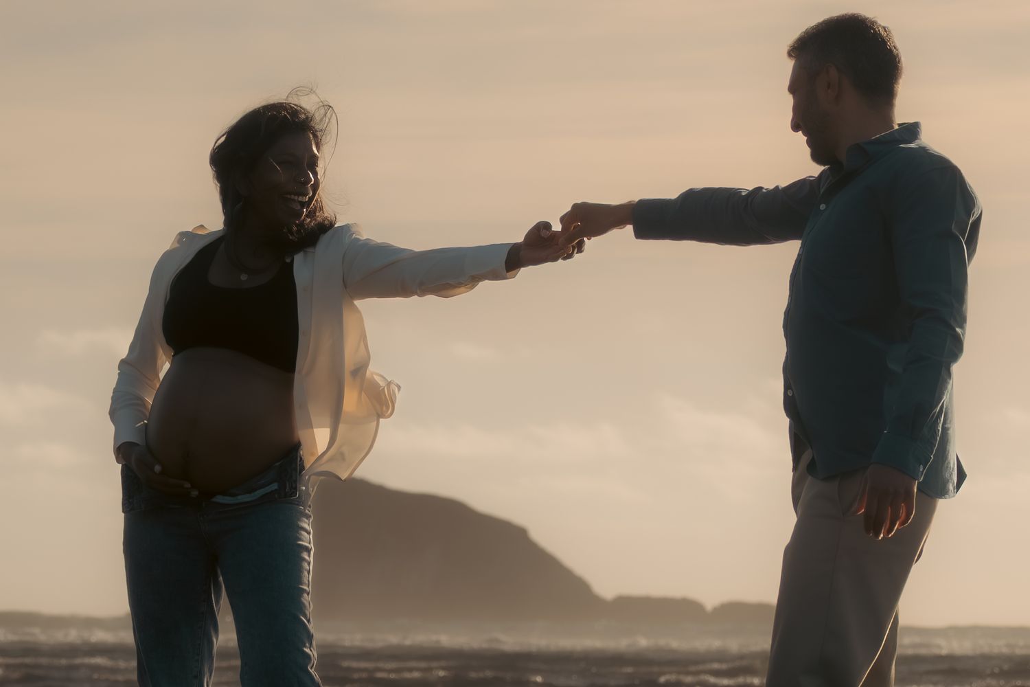 A couple stands silhouetted against a sunset sky on a beach, creating a romantic scene at dusk.